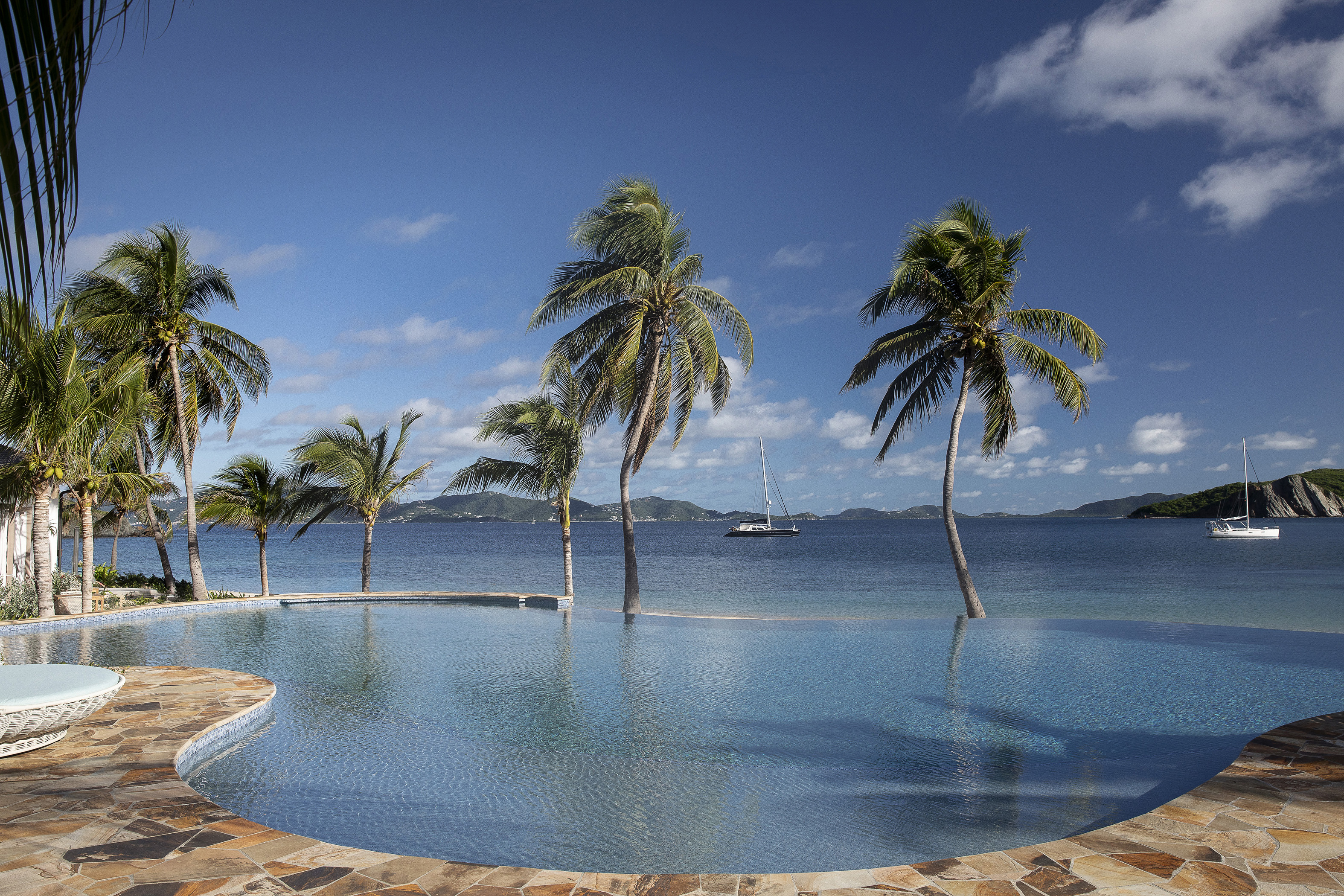 Infinity pool flanked by palm trees beside a yacht studded bay