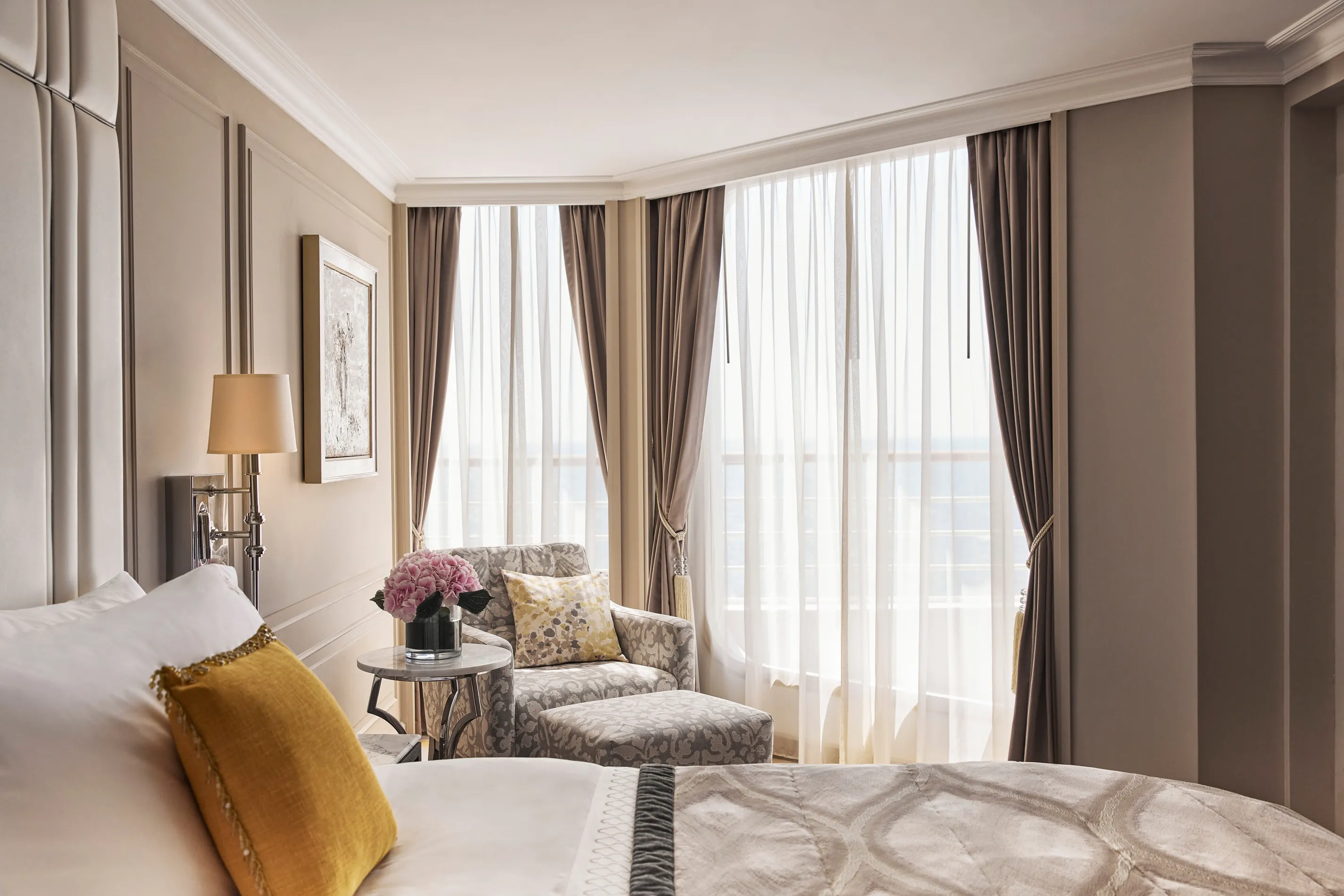 Luxurious Crystal cruise suite with a large bed, elegant furnishings, and floor-to-ceiling windows letting in soft natural light.