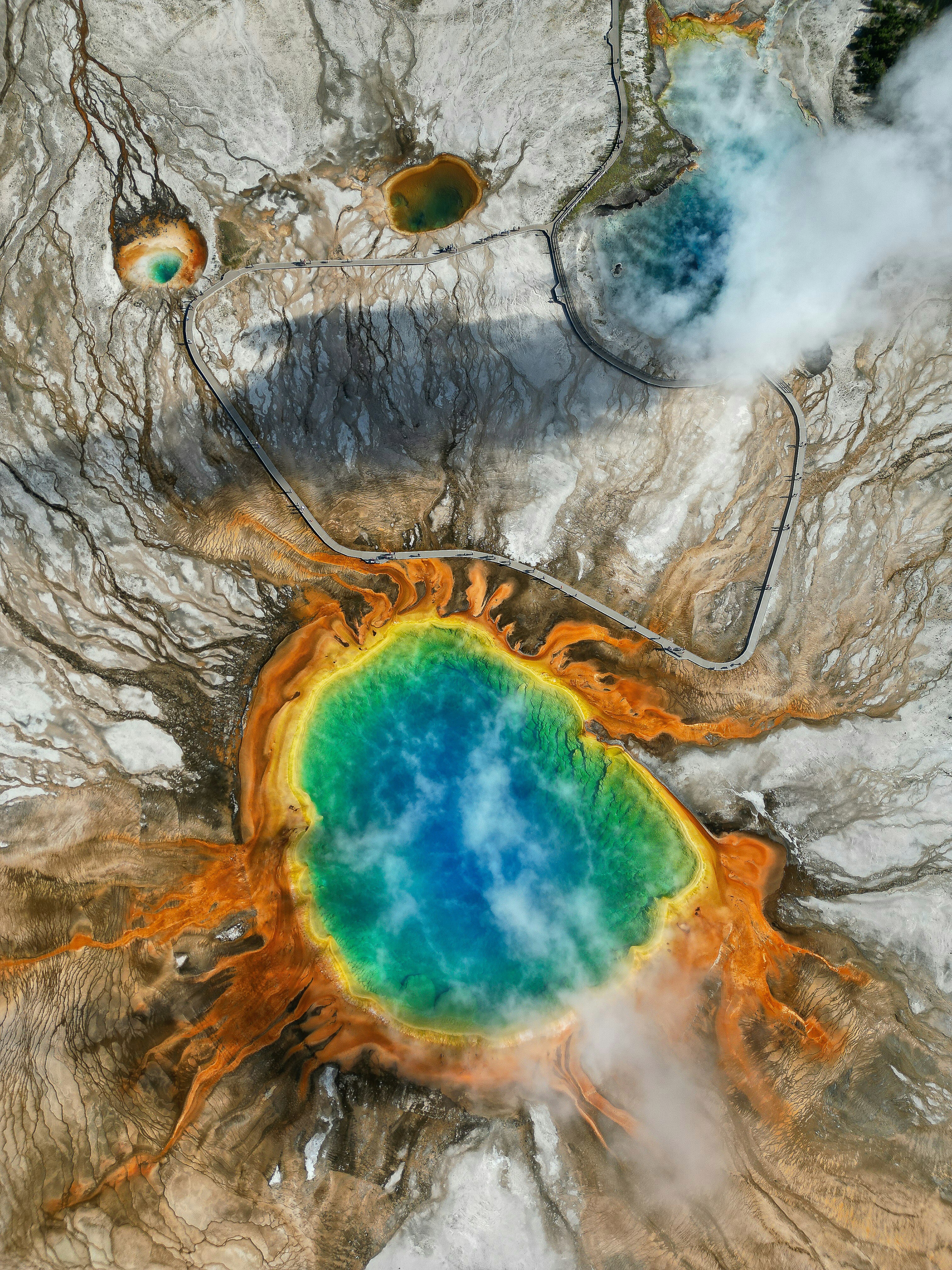 A bird's-eye view of a geyser in Yellowstone National Park where a blue pool is surrounded by red and yellow earth