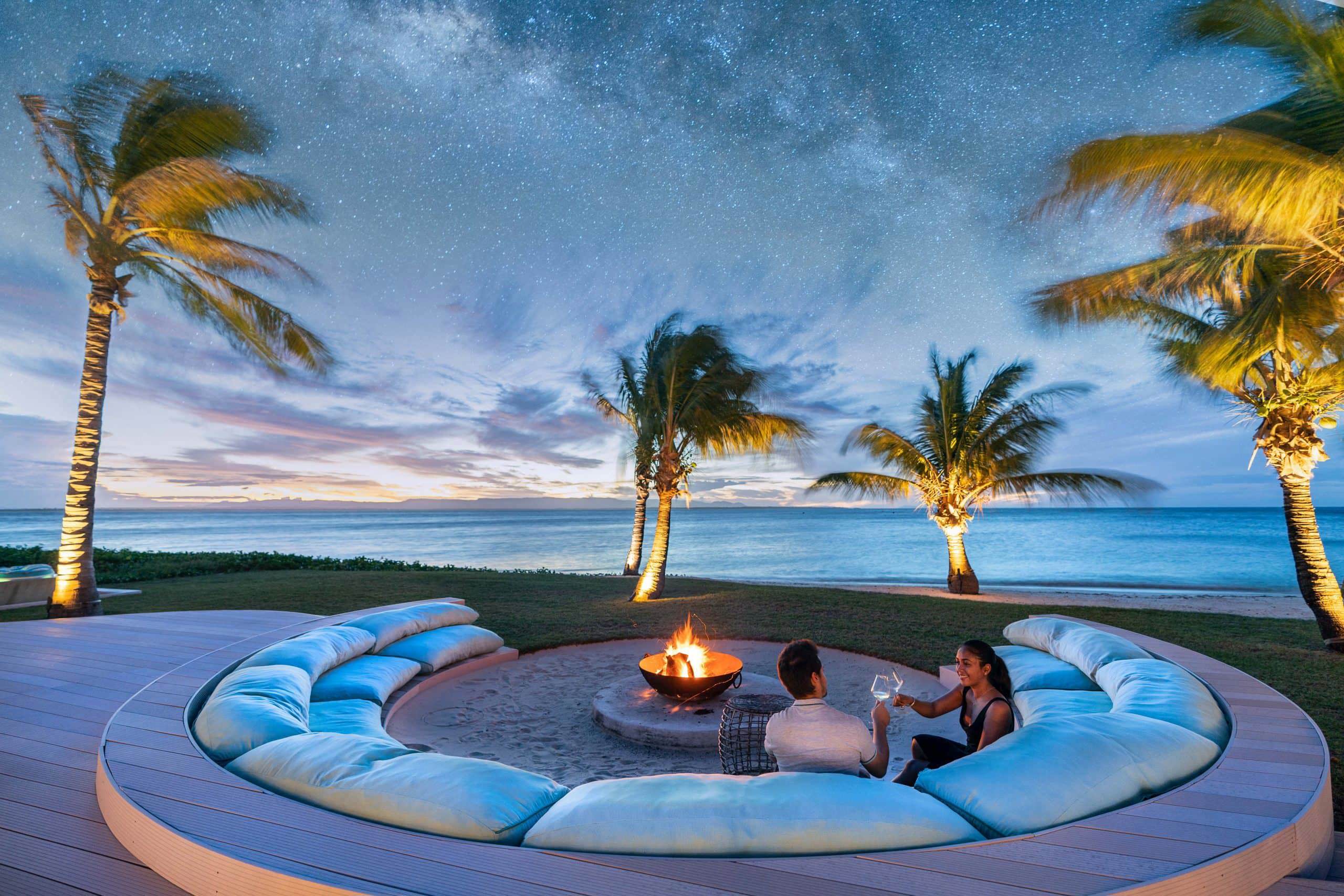 Couples having sundowners around the firepit surrounded by palm trees