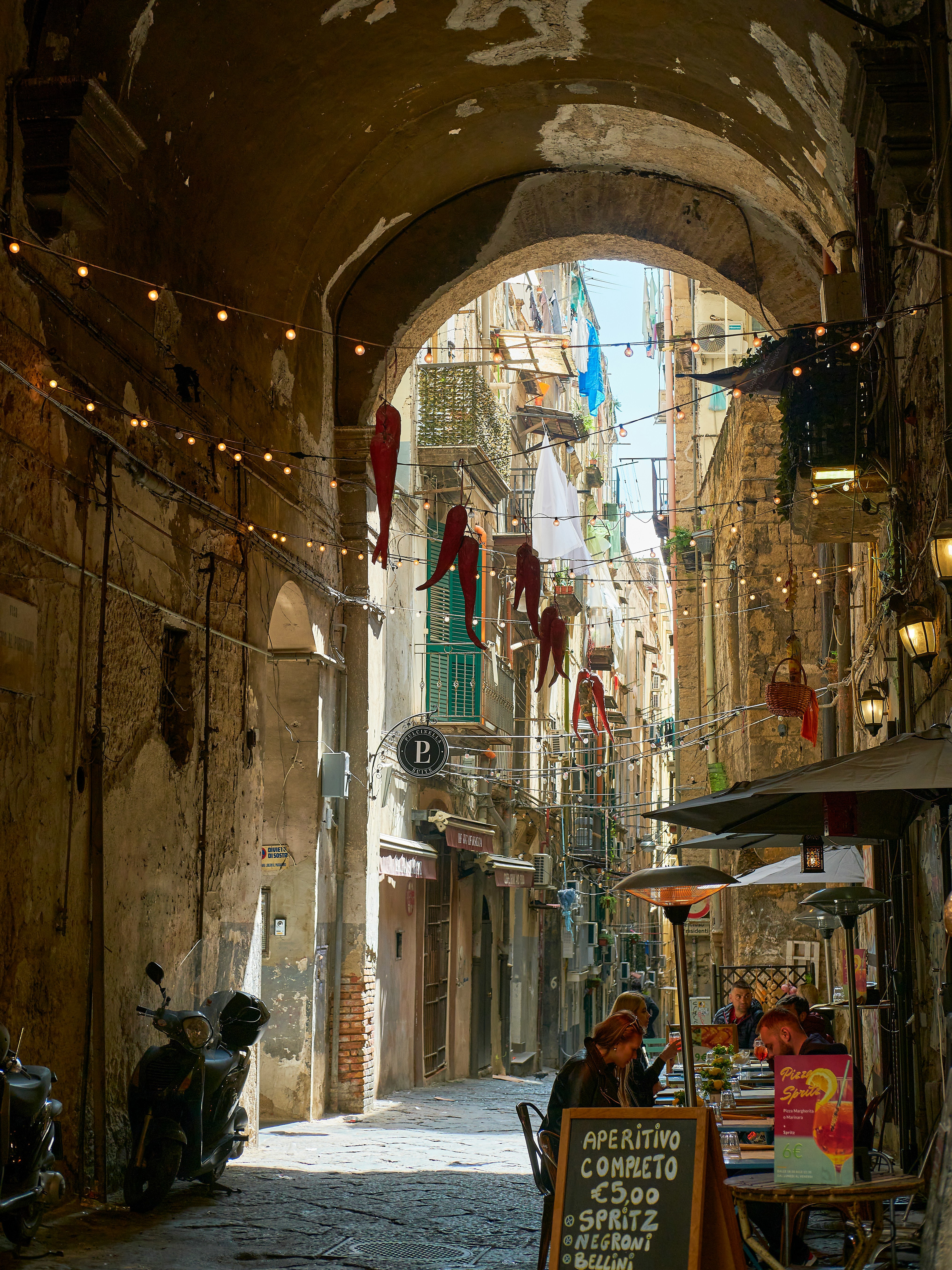 Charming narrow street in Naples with outdoor café seating under an archway and hanging decorations.
