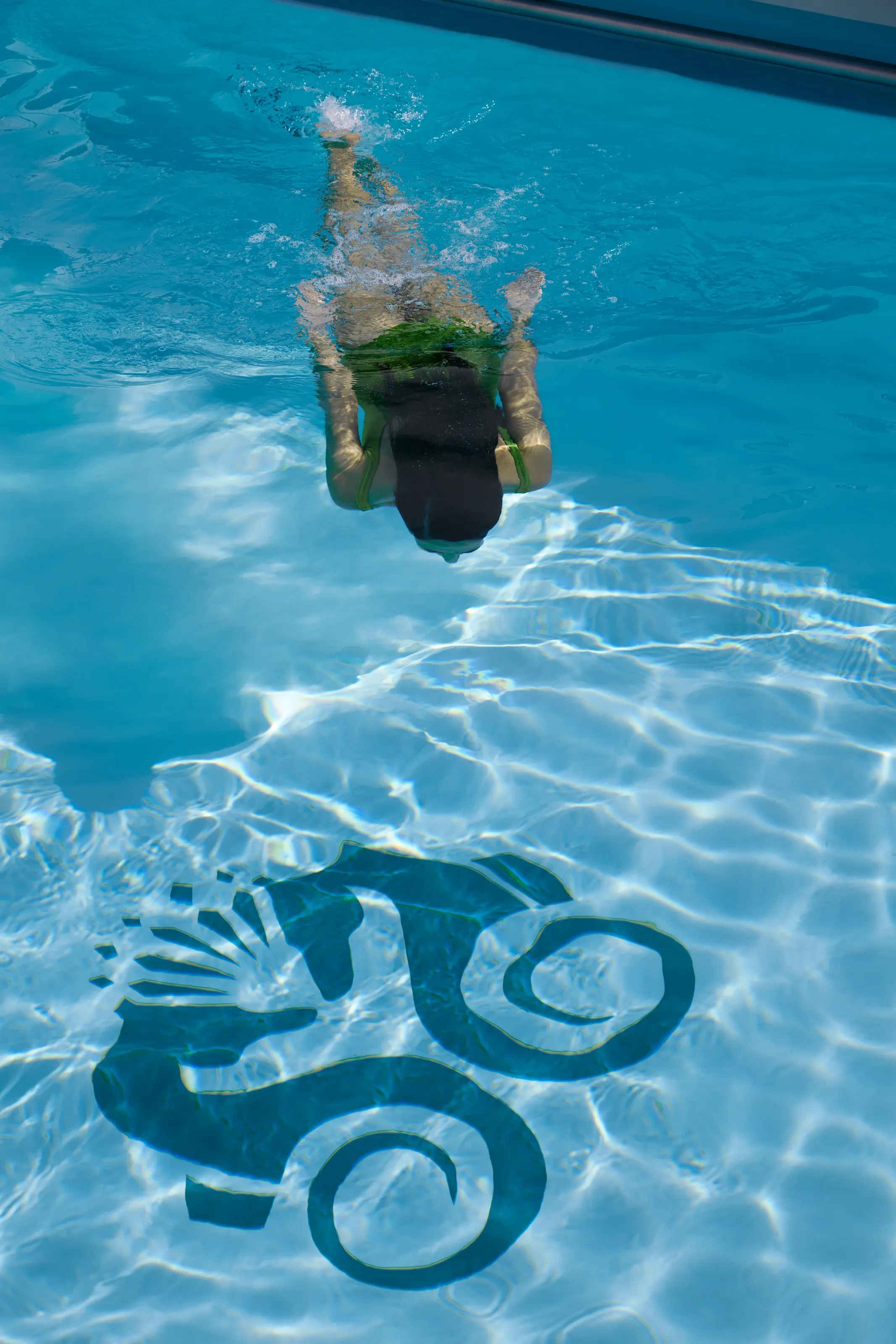 Underwater view of a swimmer in a Crystal Cruises pool featuring a large decorative seahorse design on the floor.