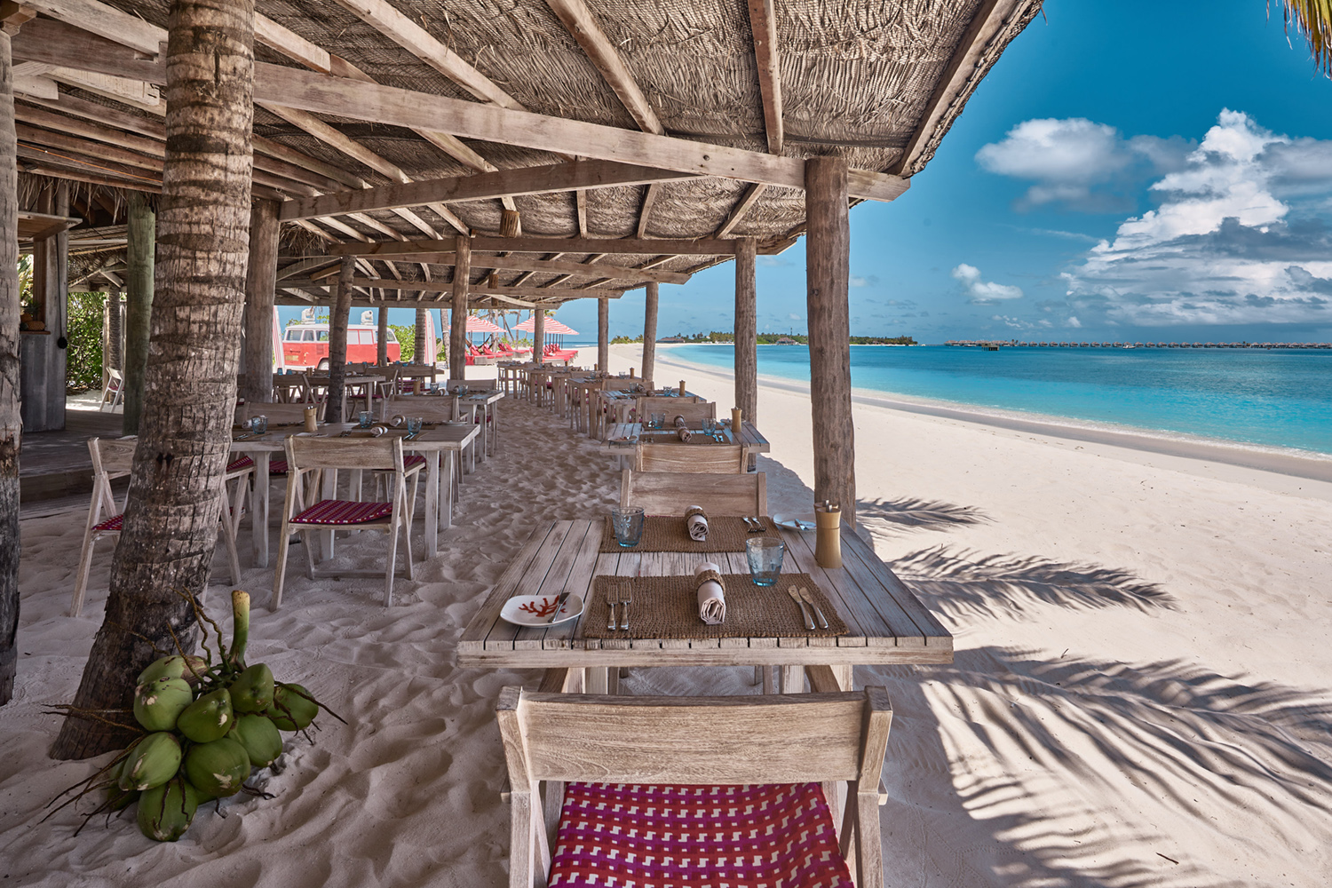 Tables and chairs of the Crab Shack at Finolhu shaded from the sun by a thatched gazebo by the ocean