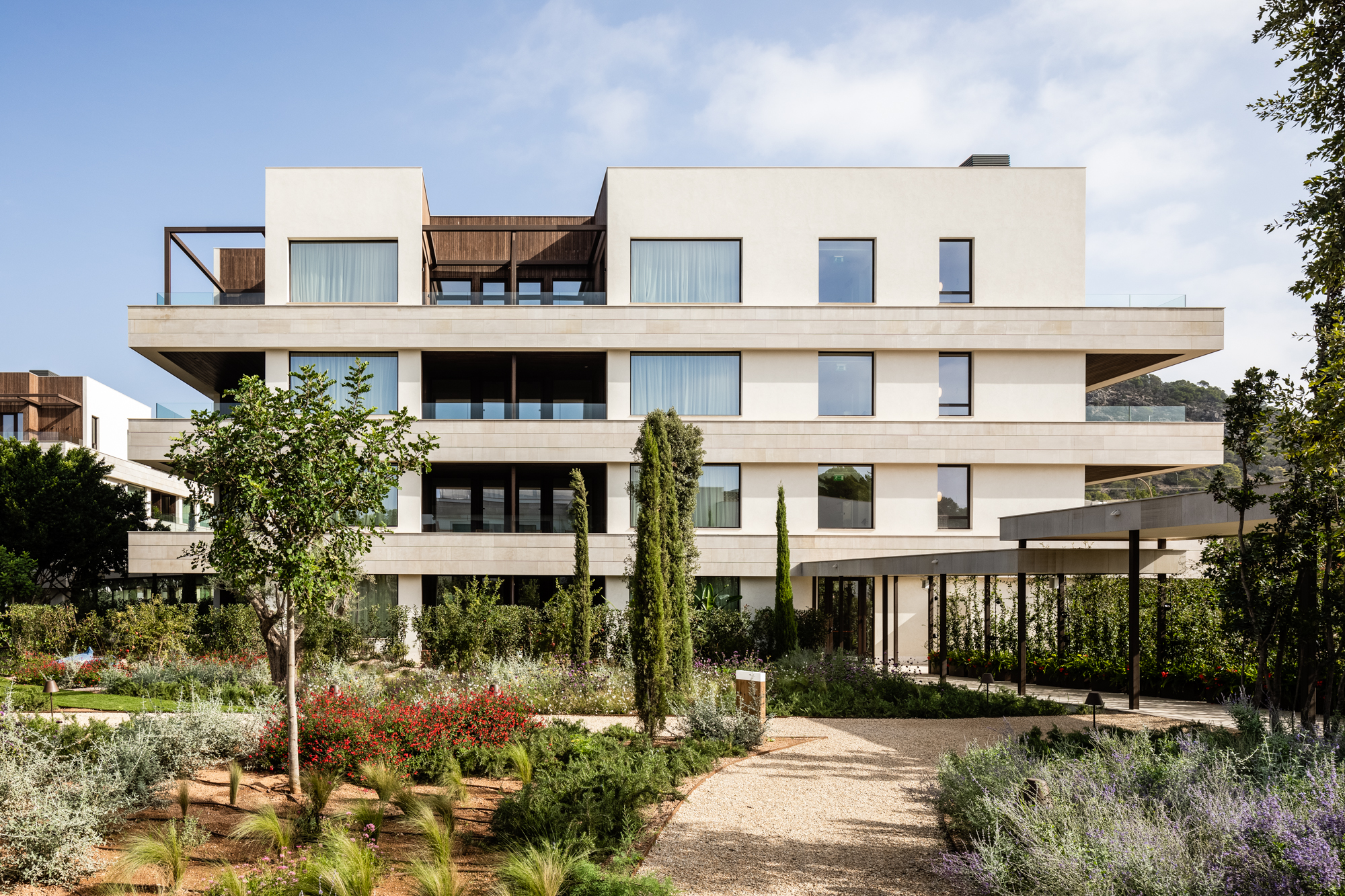 A modern multi-story residential building with balconies, surrounded by a landscaped garden.