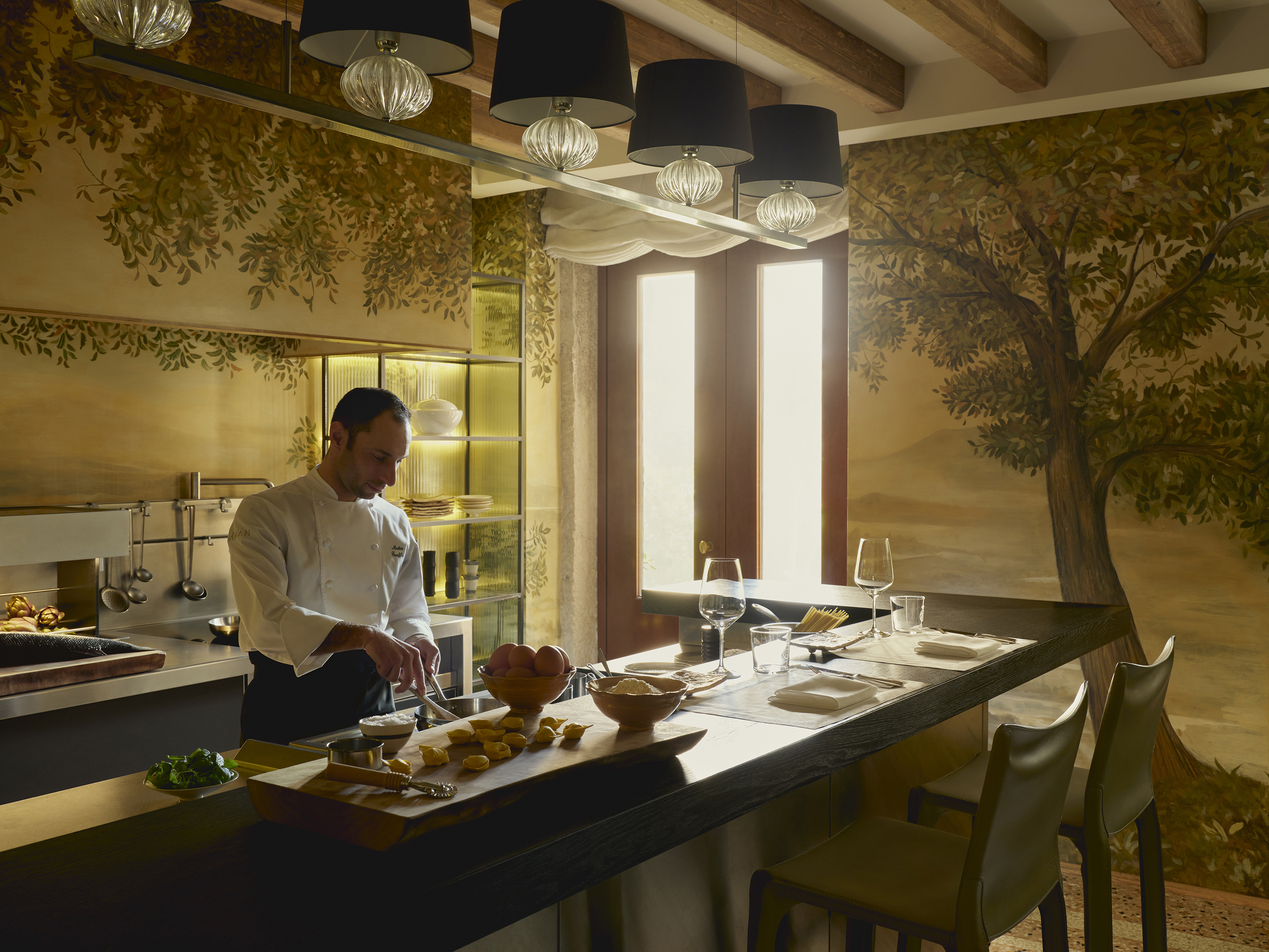 An intimate open kitchen with a chef preparing food beside two dining sets