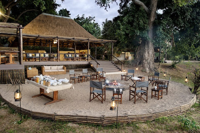 The raised sandy outdoor breakfast area of Chiawa Camp featuring tables set for breakfast before a thatched roofed building