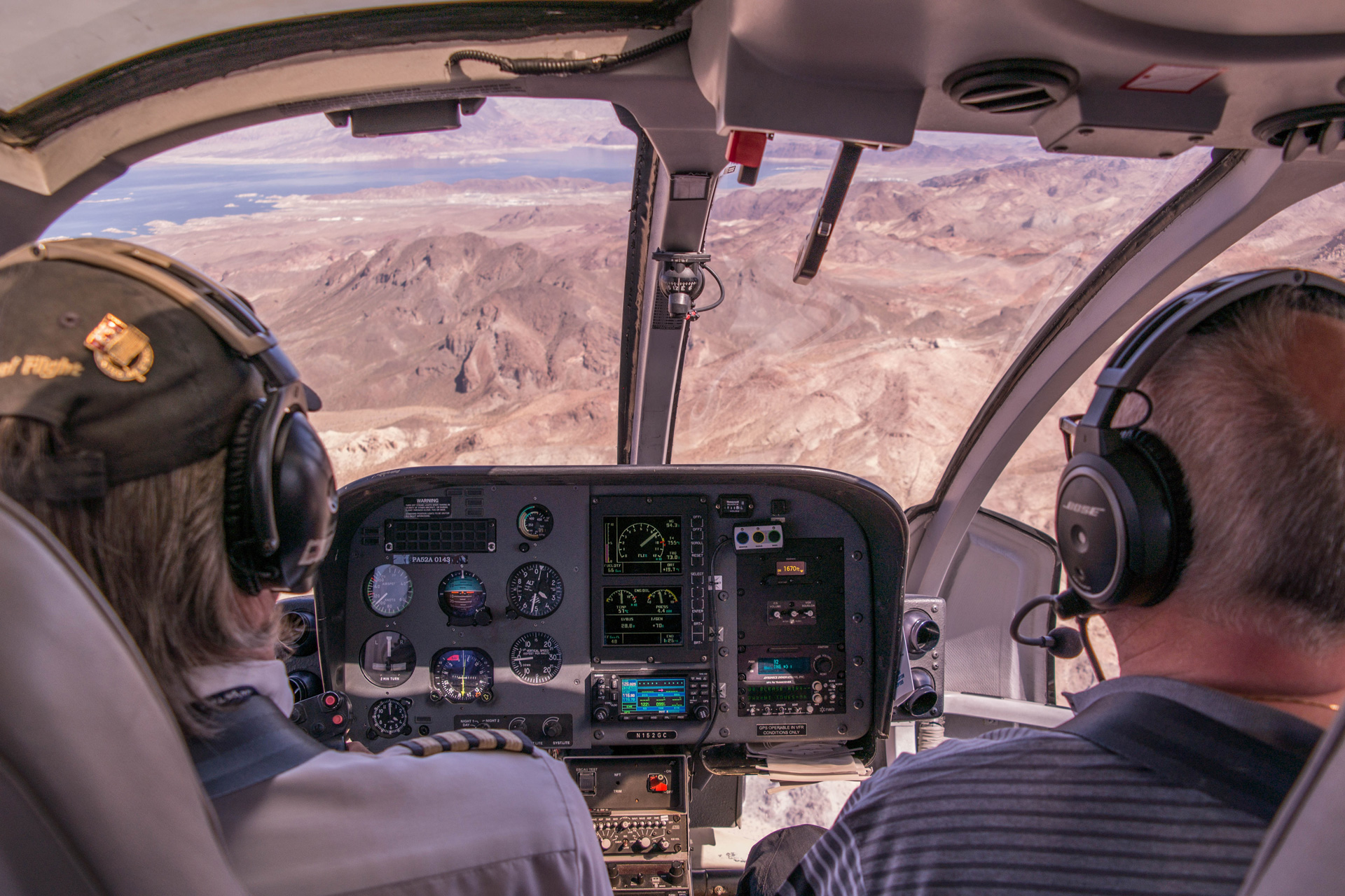 Two people in the front seats of a helicopter looking out to the grand canyon