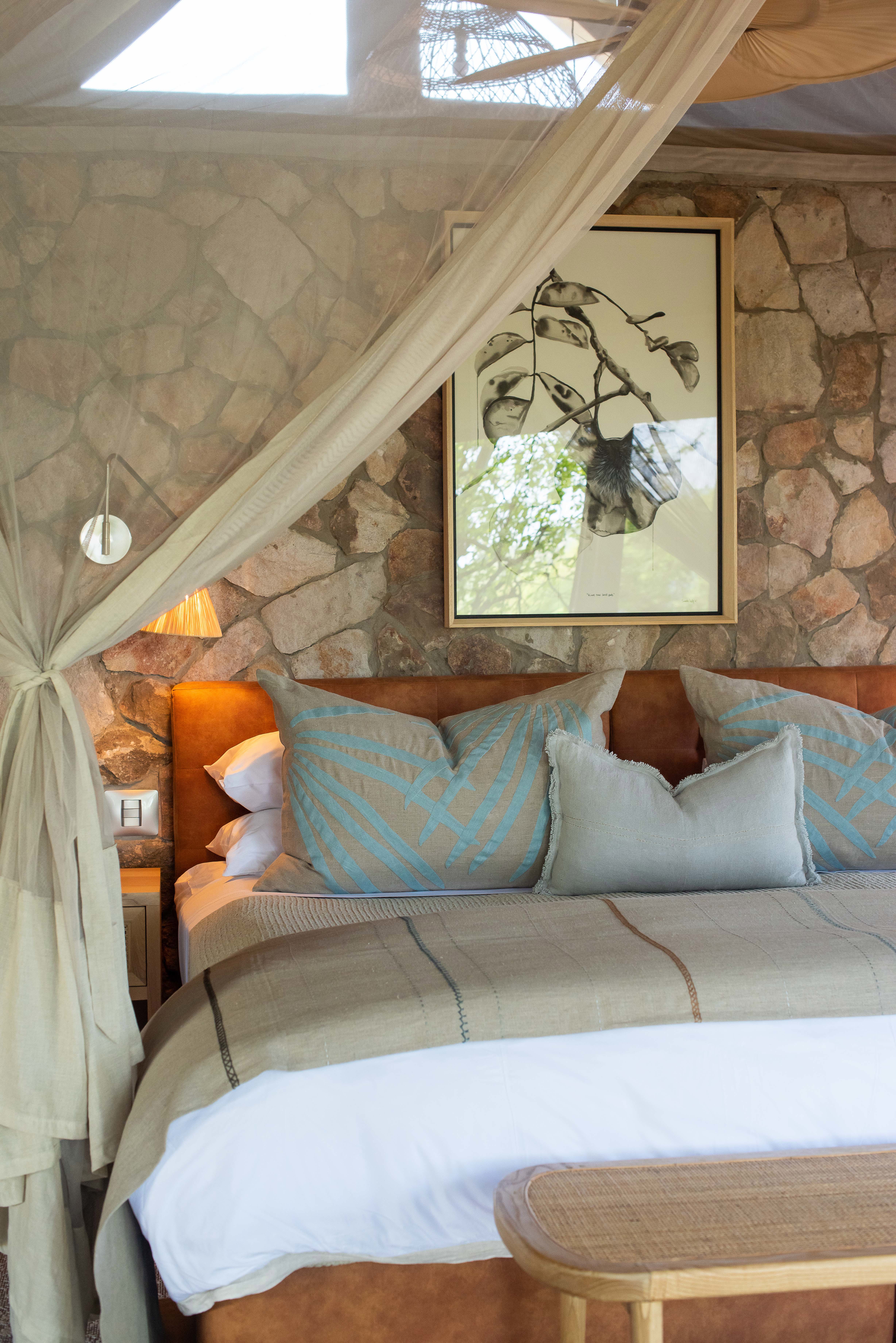 A plush canopy bed with comfy pillow and cushions pushed against a stone wall with artwork
