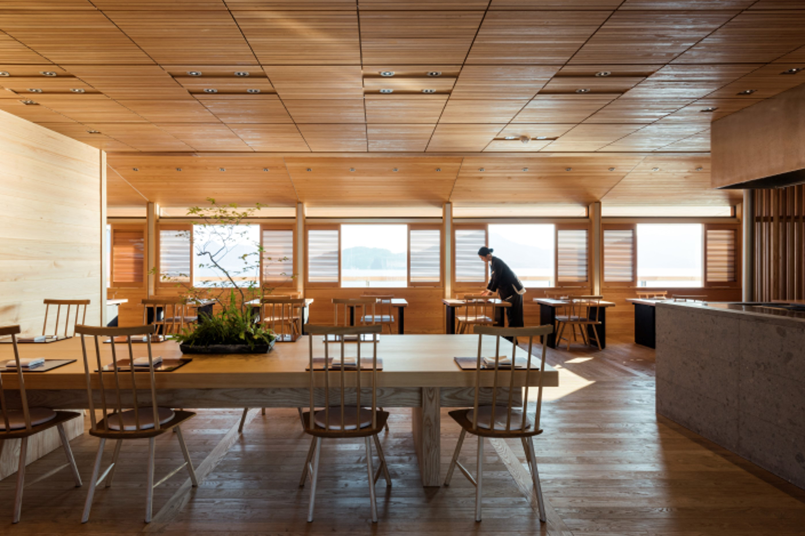 A minimal wooden dining room aboard Guntu with a waitress setting tables 