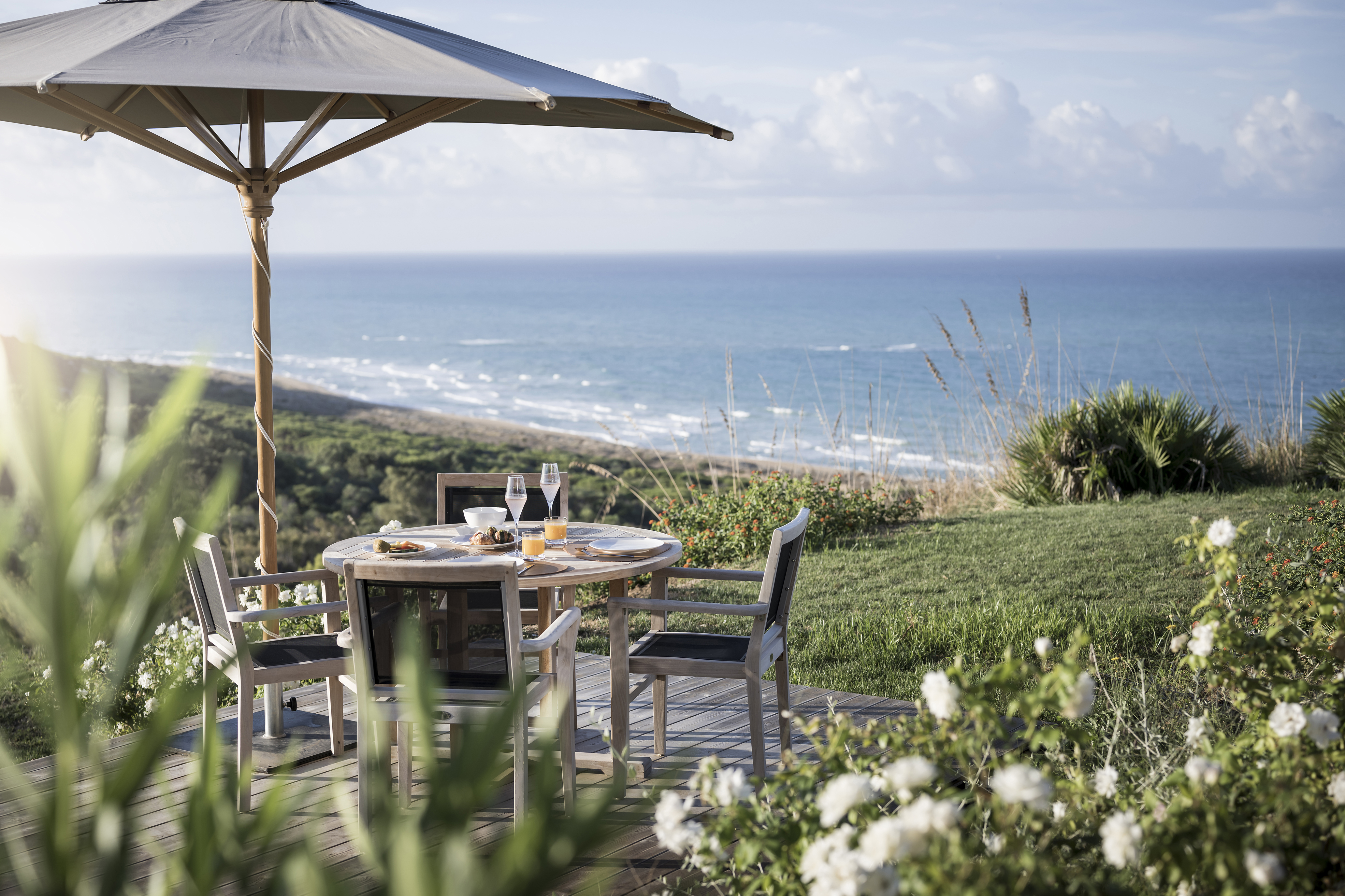 Patio furniture and umbrella set on a small wooden terrace on a lawn overlooking the sea
