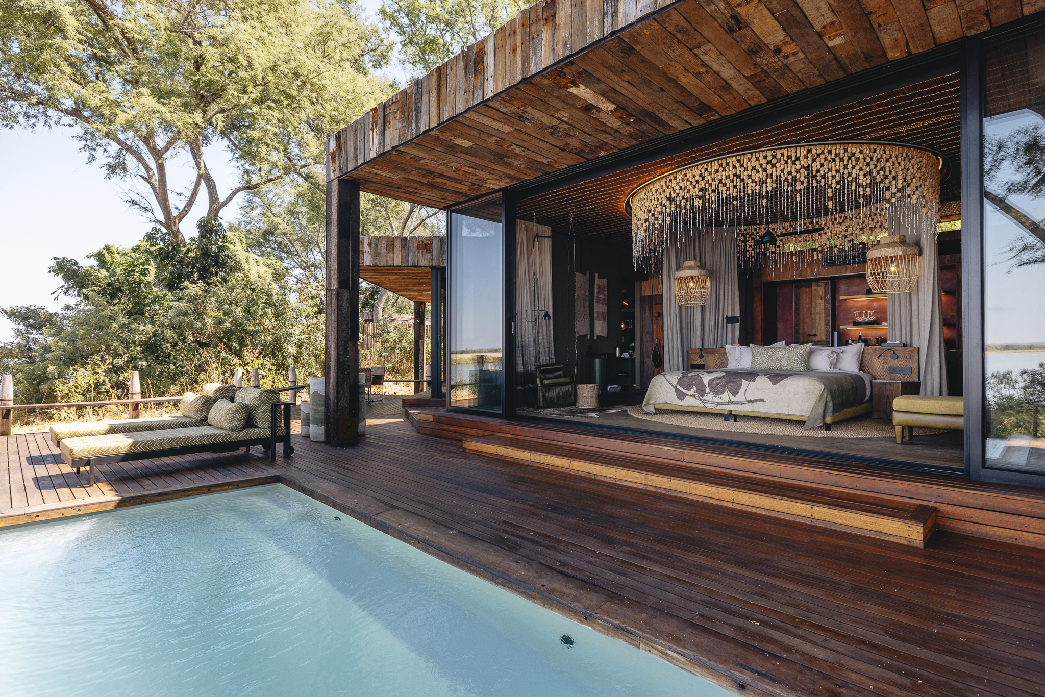 The outside of a large suite featuring a plunge pool and loungers, with a glimpse of a bedroom inside featuring a large bed with circular decor above 