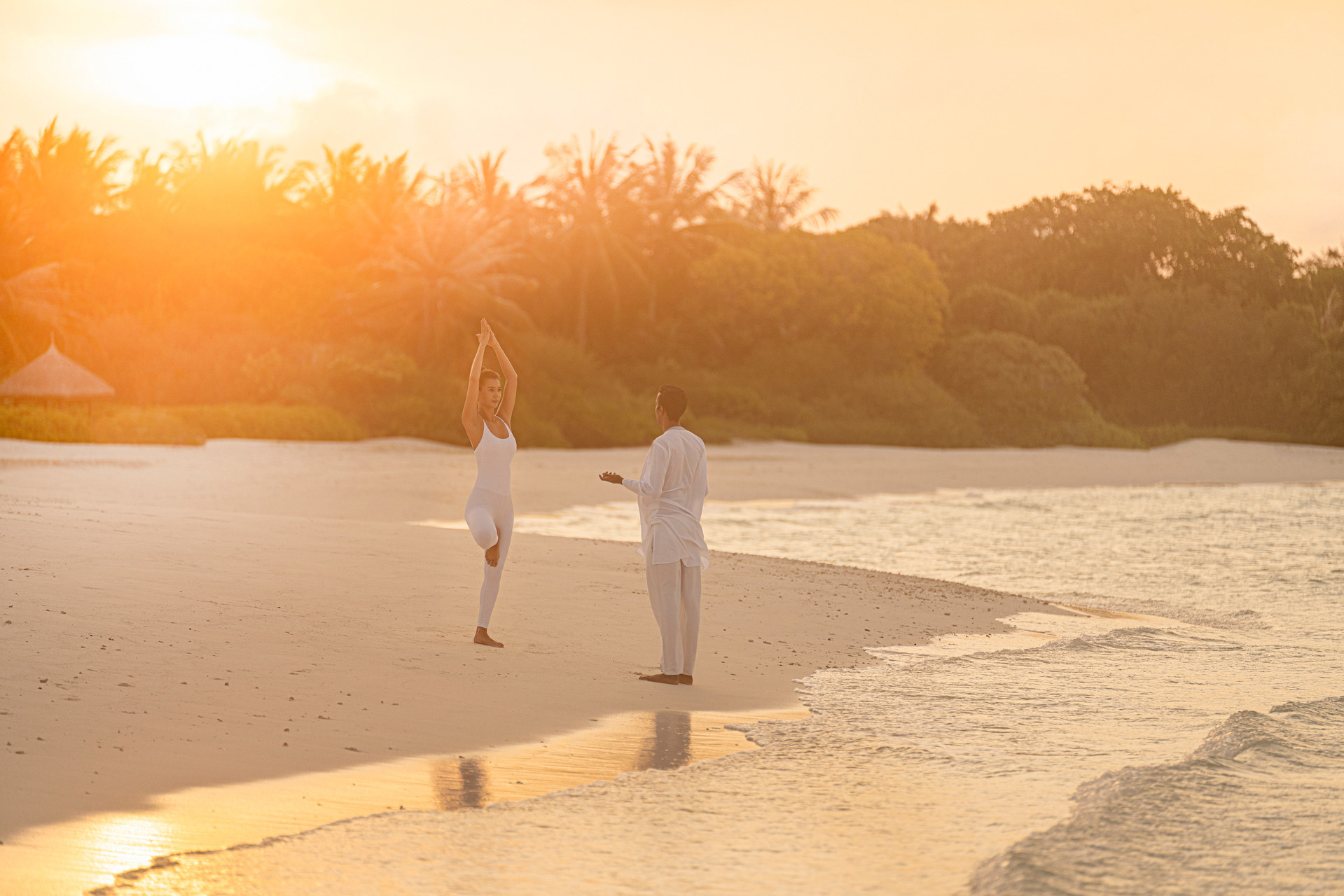 Woman practicing yoga on the beach at sunset with an instructor 