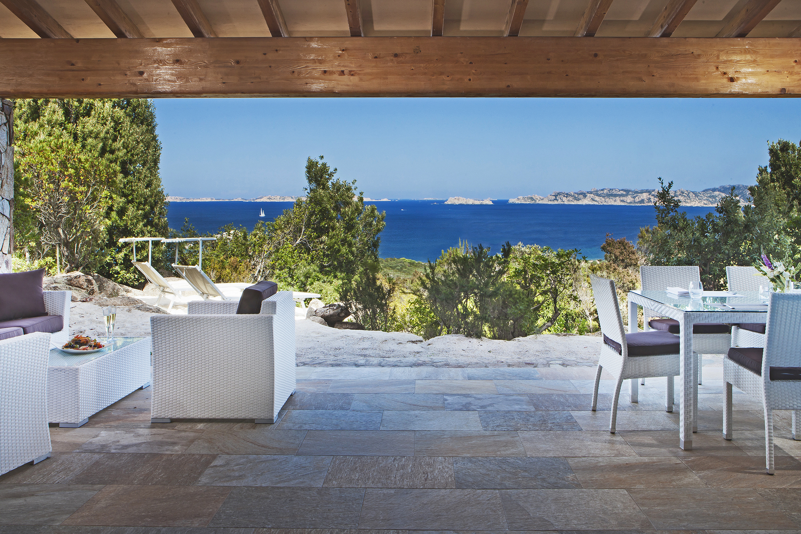The stone terrace of Suite Arcipelago at La Licciola Hotel featuring white rattan furniture and ocean views