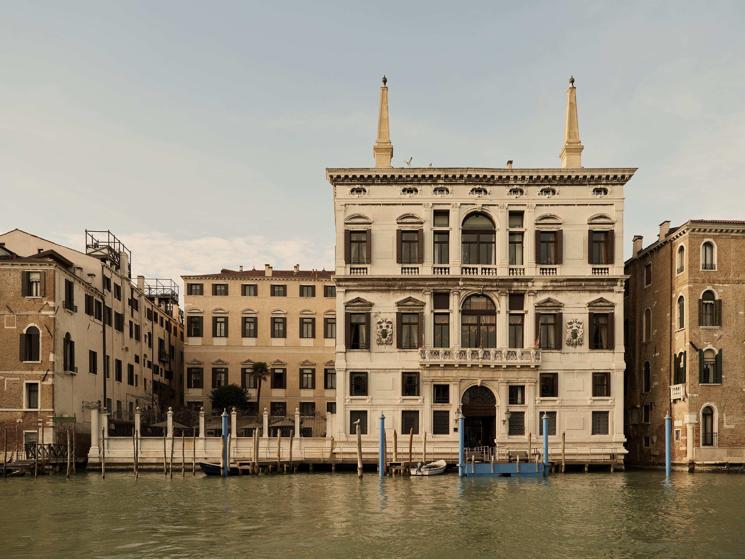 A grand white Venetian palazzo with lots of windows surrounded by smaller buildings and fronted by water