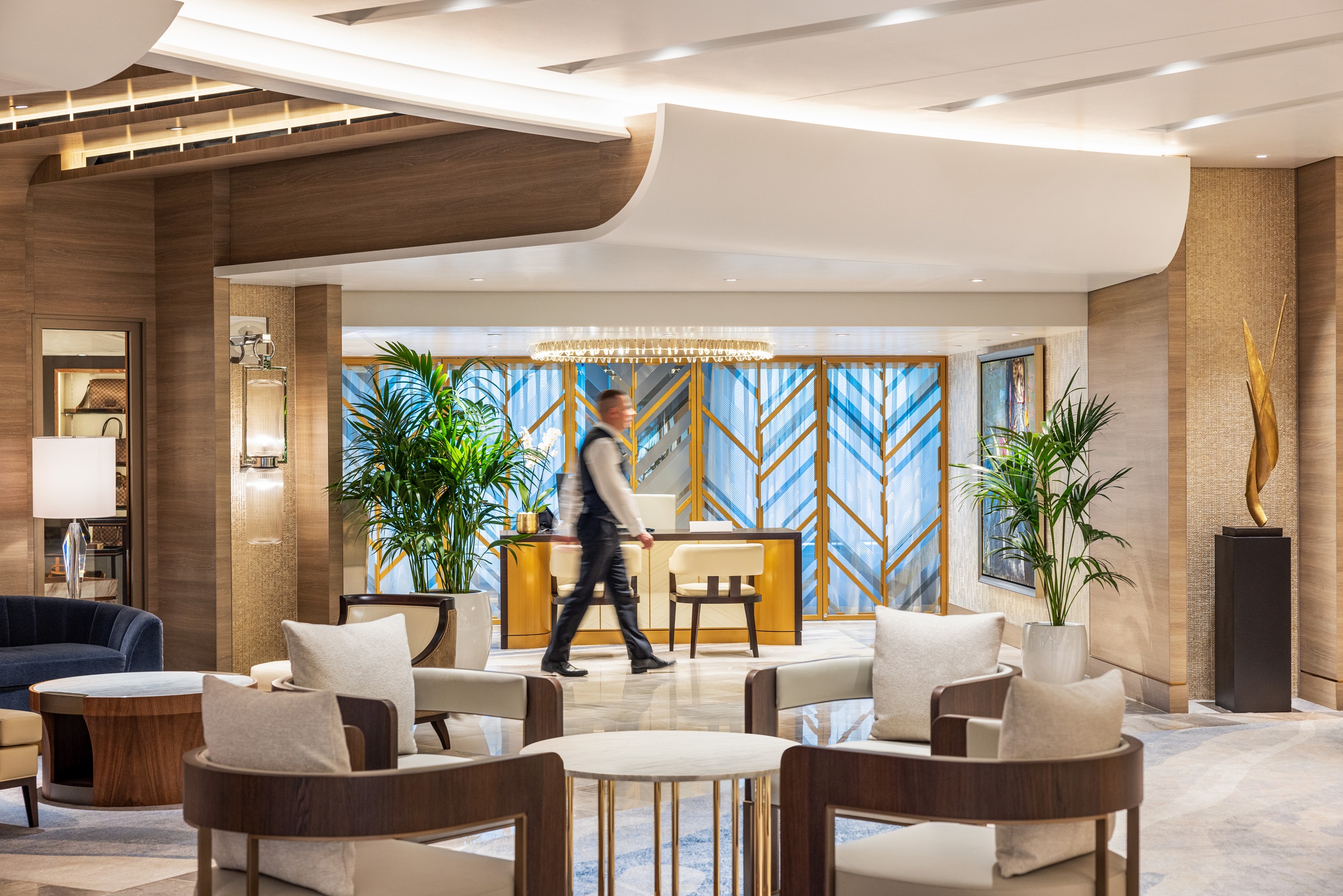 Modern Oceania Cruises atrium with stylish furniture, a person walking, and a reception desk in the background.