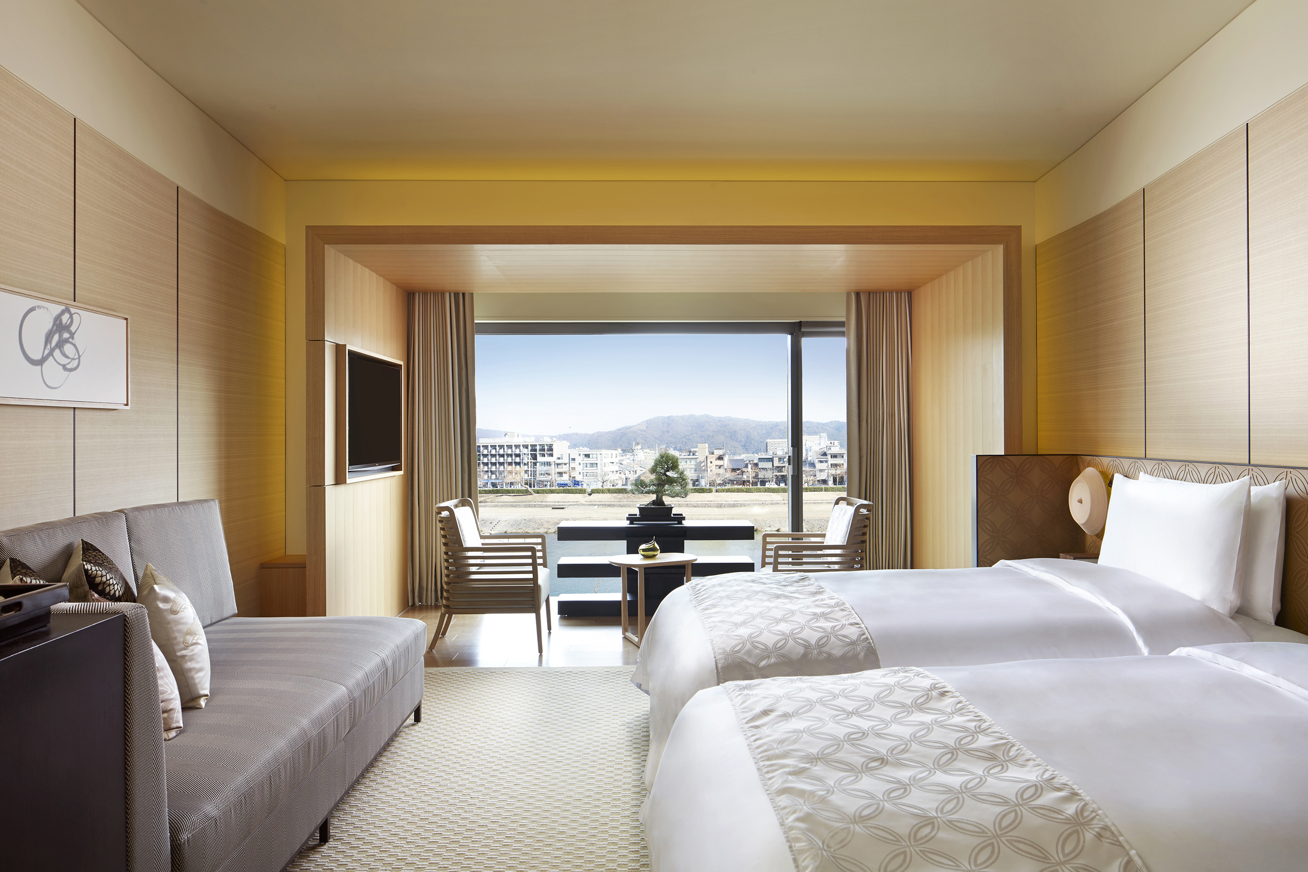 A light and siry suite featuring two comfy beds, a plush sofa and dining table overlooking a view of Kyoto