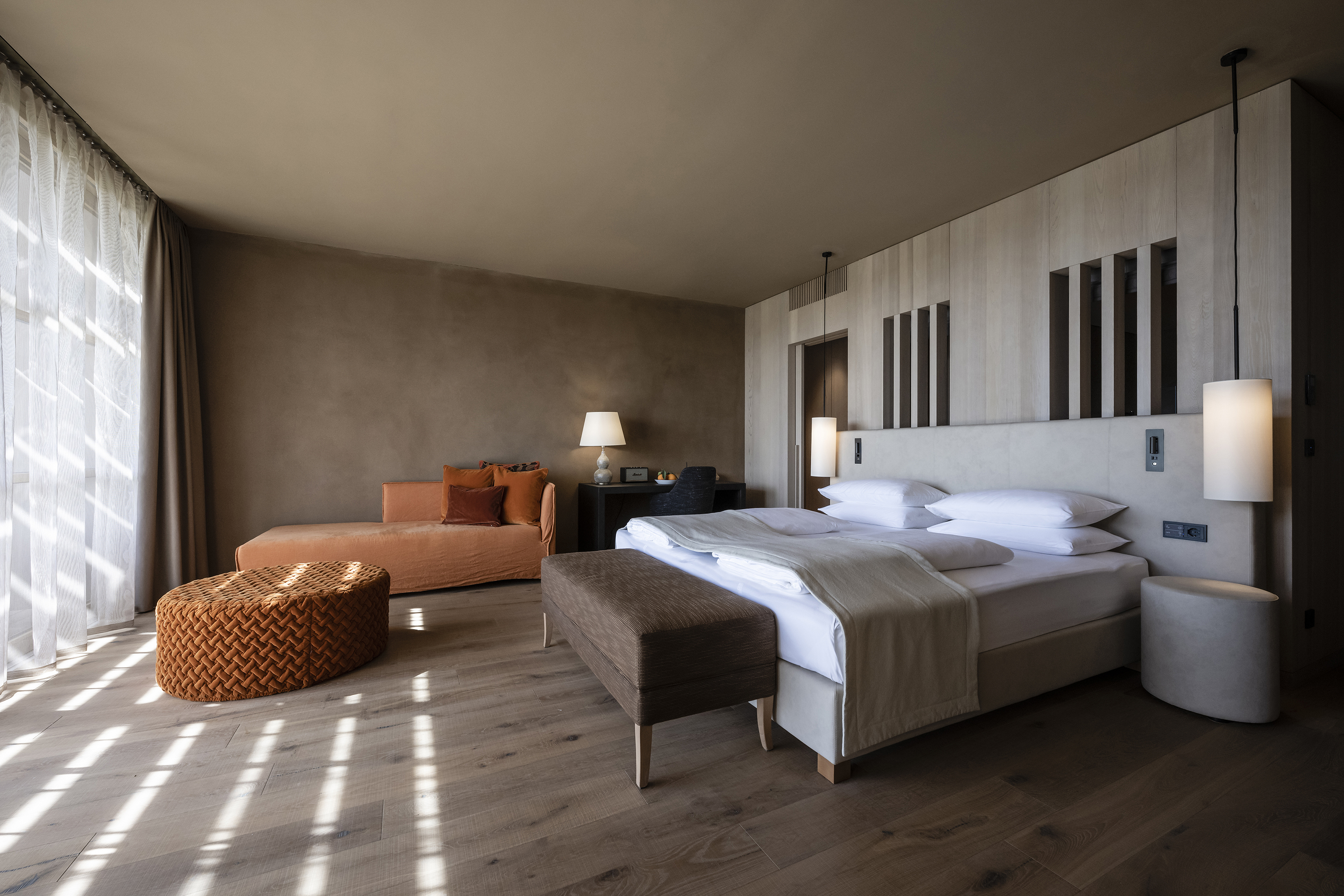 Neutral bedroom in earthy tones with orange sofa and white bed