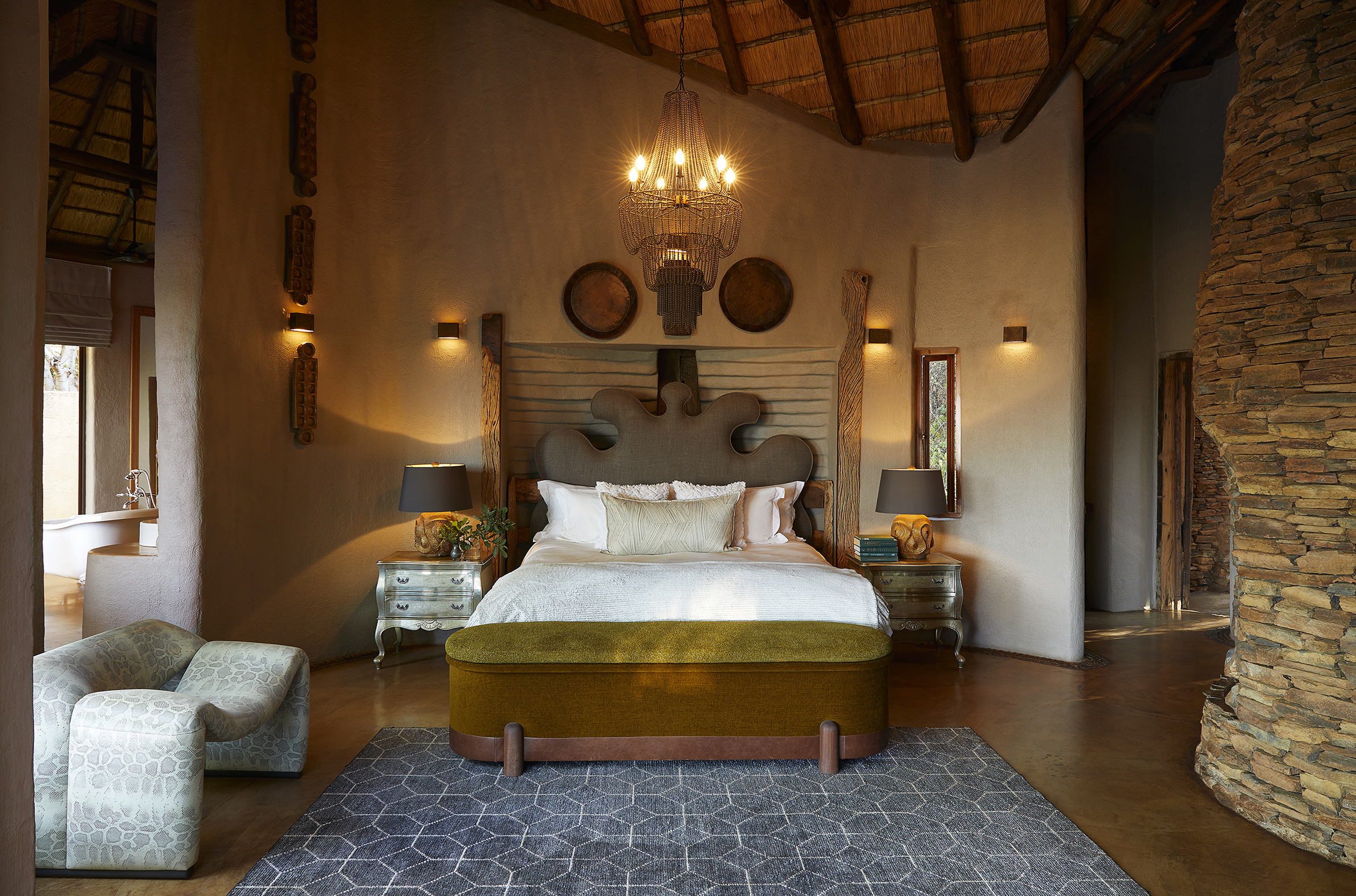 A tall stylish bedroom at Molori Lodge decorated in safari-style furniture featuring a plush bed and wooden wall decor