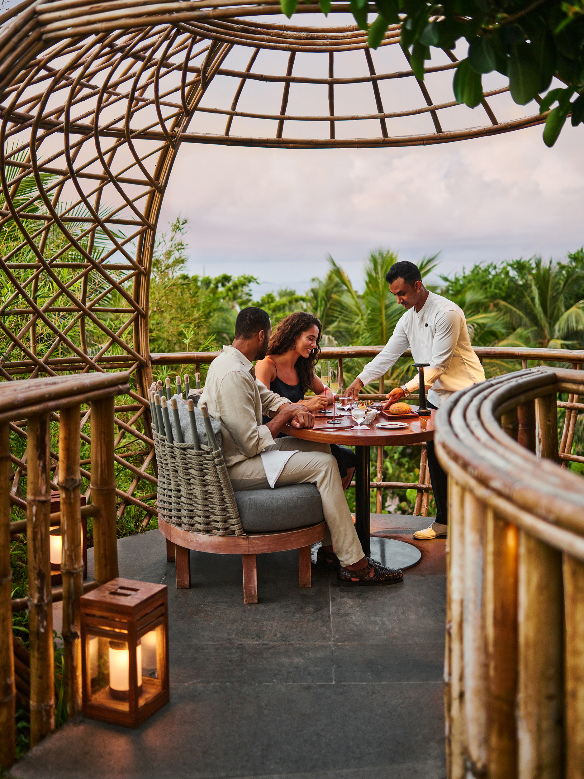 A couple having a private dining experience in a tree house pod while a waiter serves their dishes