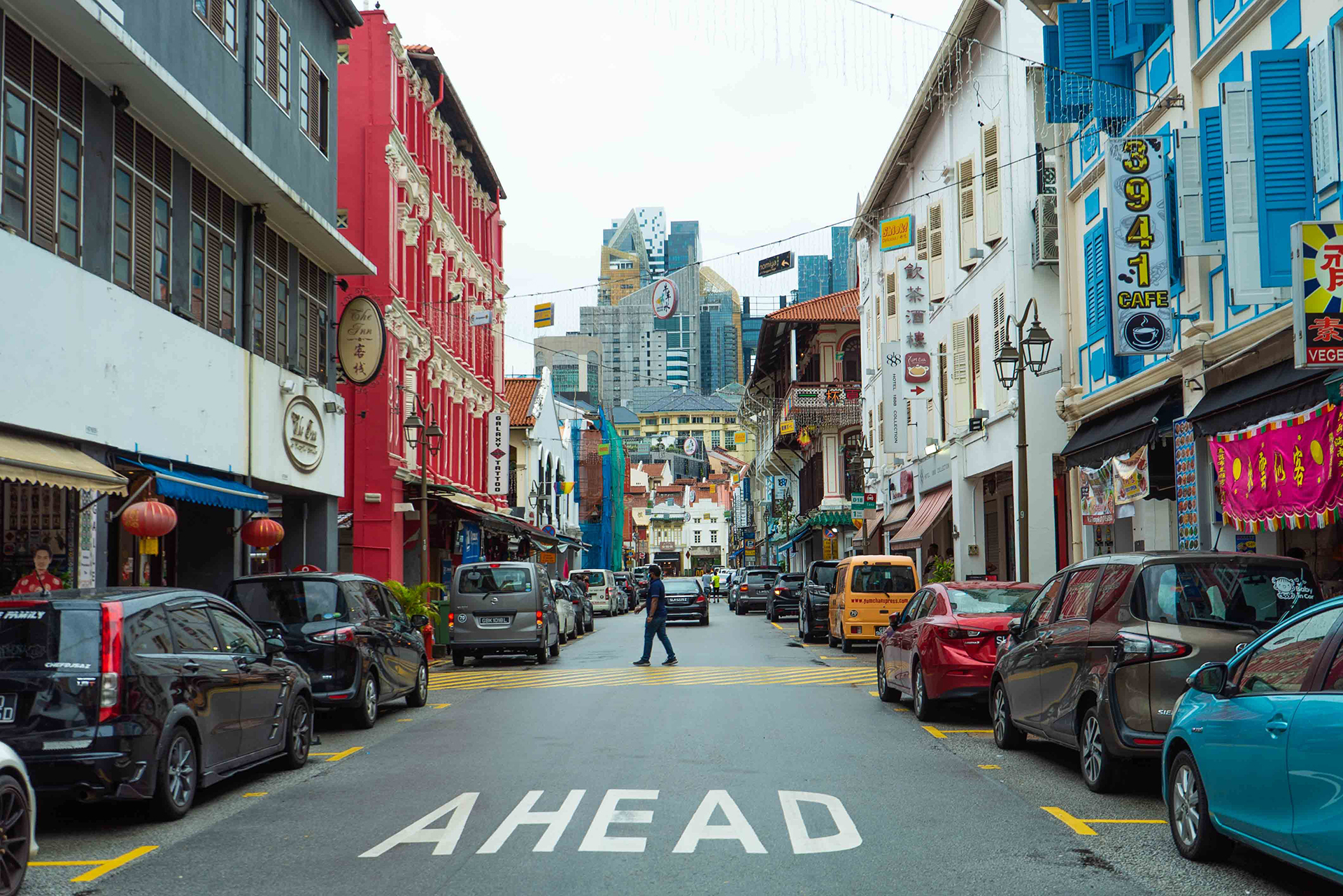 A man crossing a street in Singapore with cars parked on both sides of it
