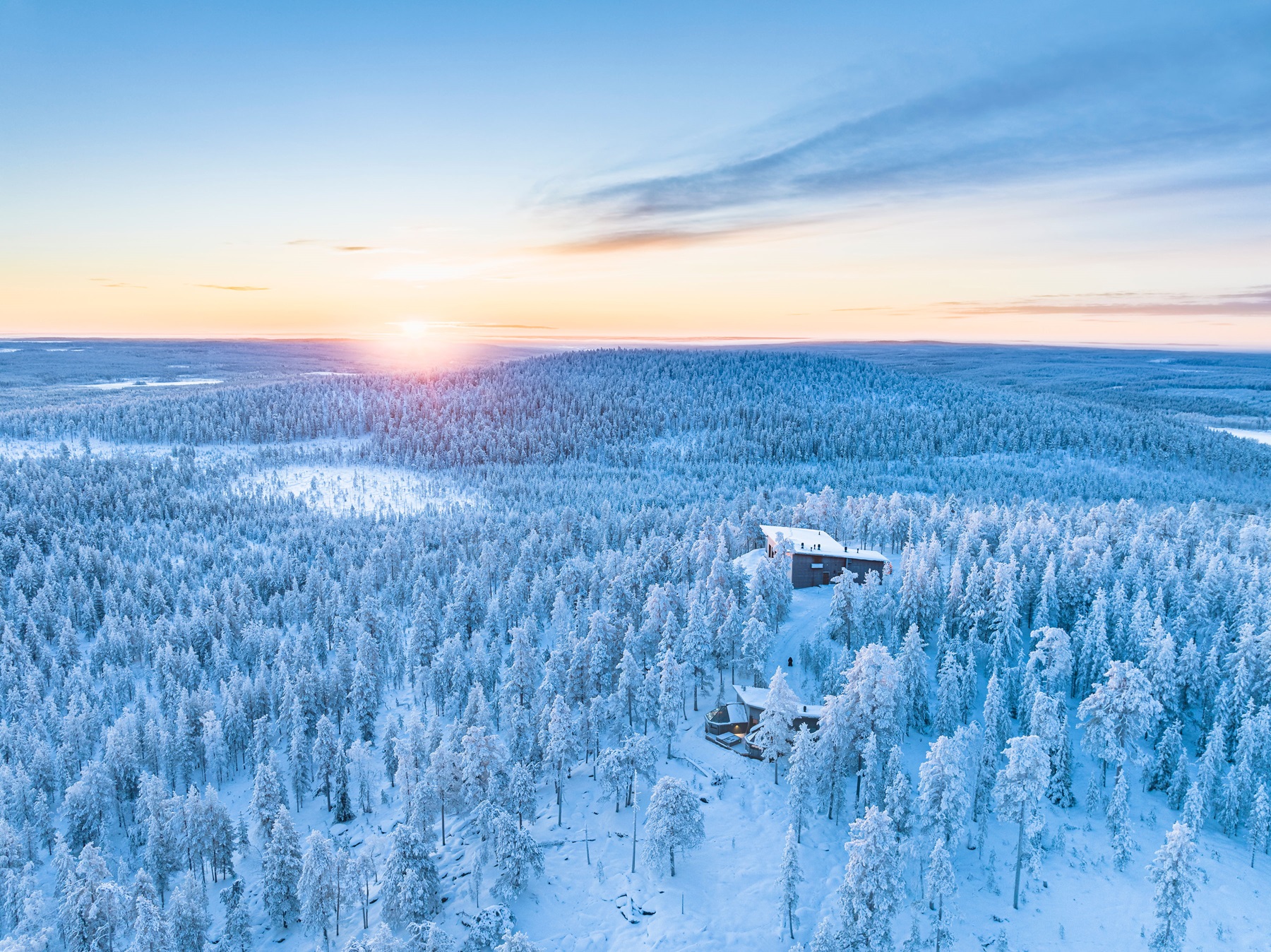 A snowy wilderness stretches to the horizon in Finnish Lapland, with cabins nestled among frost-covered trees at sunrise, ideal for a magical winter escape with the family.