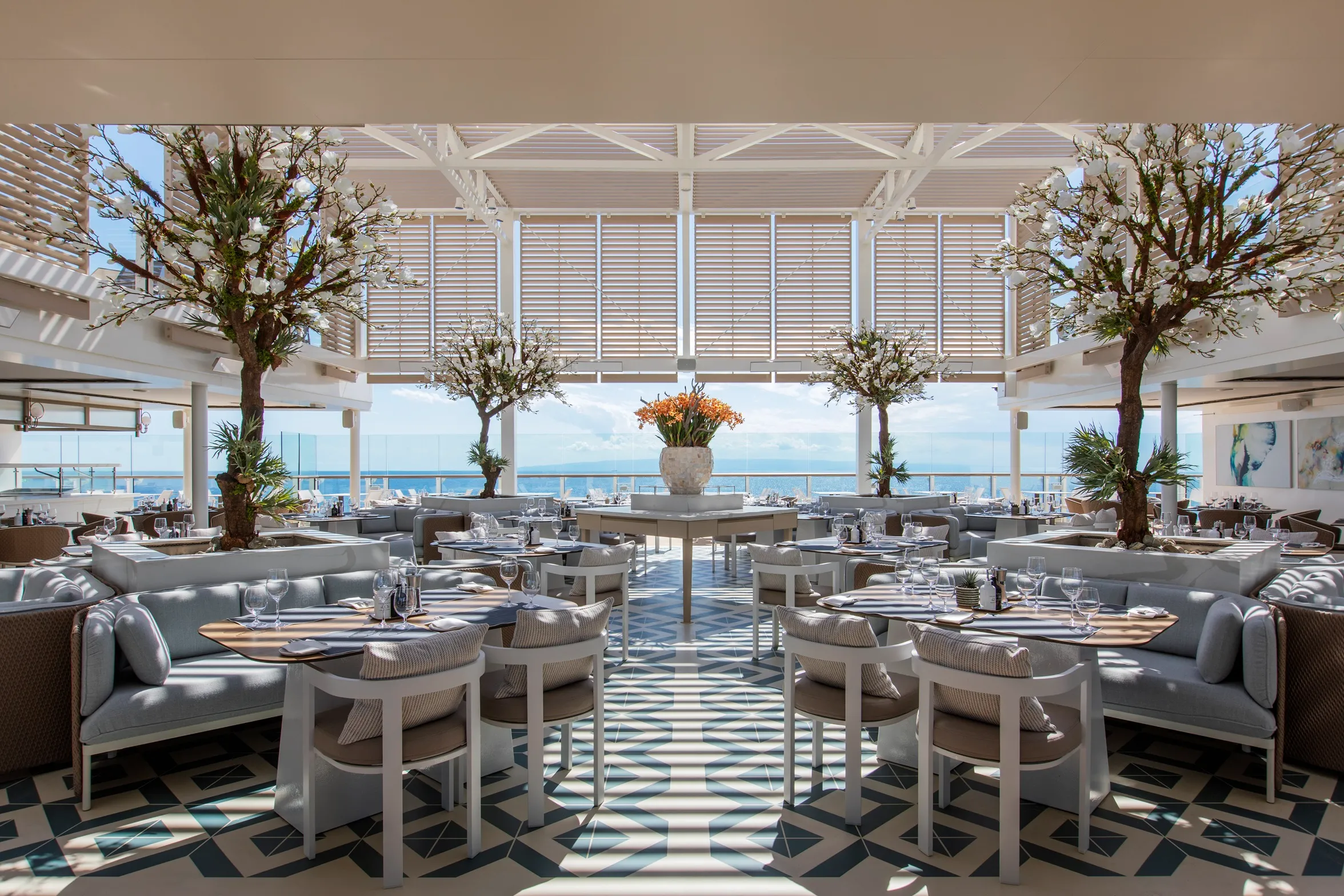 Elegant ocean-view restaurant with modern decor, round tables, white chairs, and large windows.
