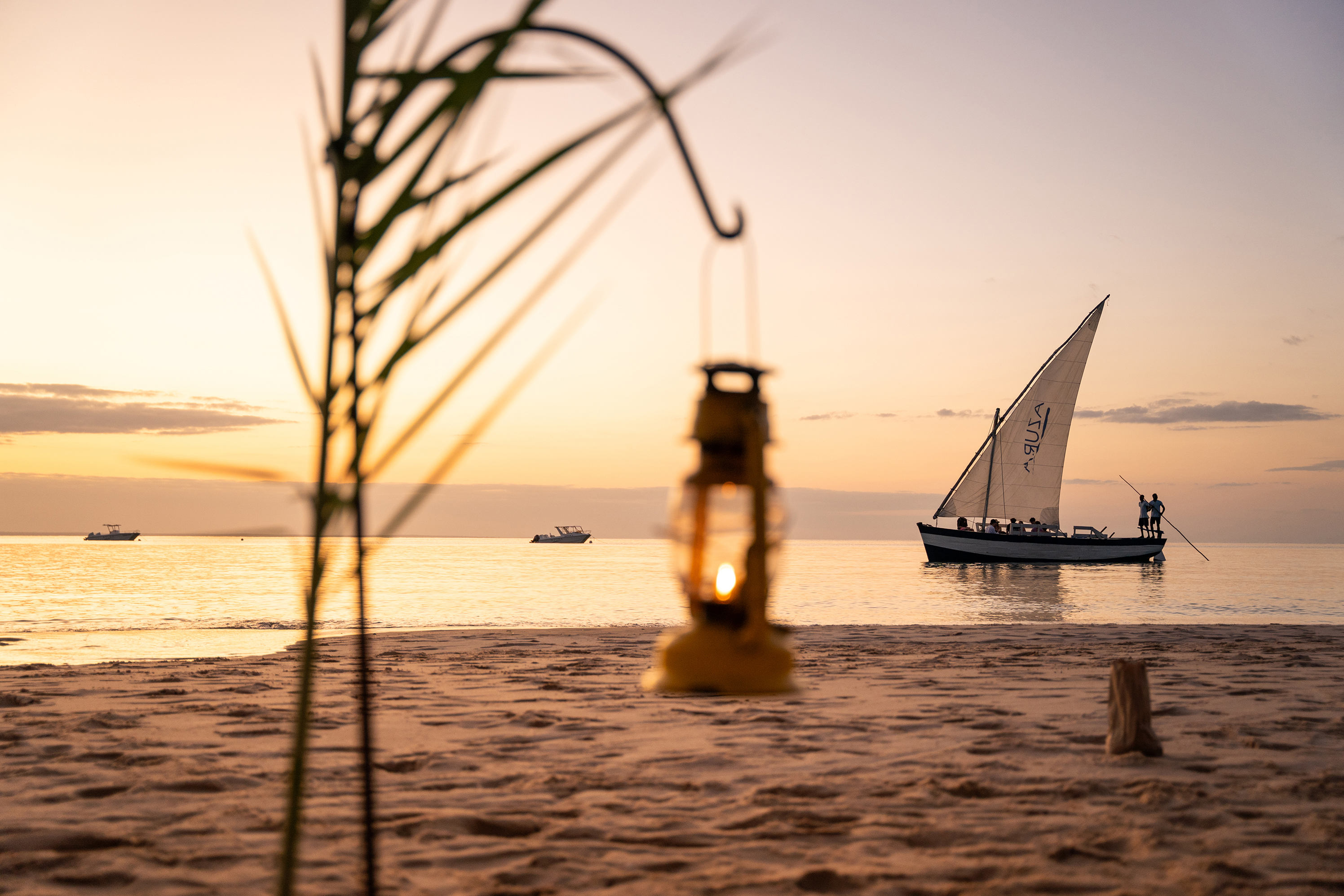 Dhow boat cruising calm waters just offshore at sunset with a hanging lantern blurred in the foreground