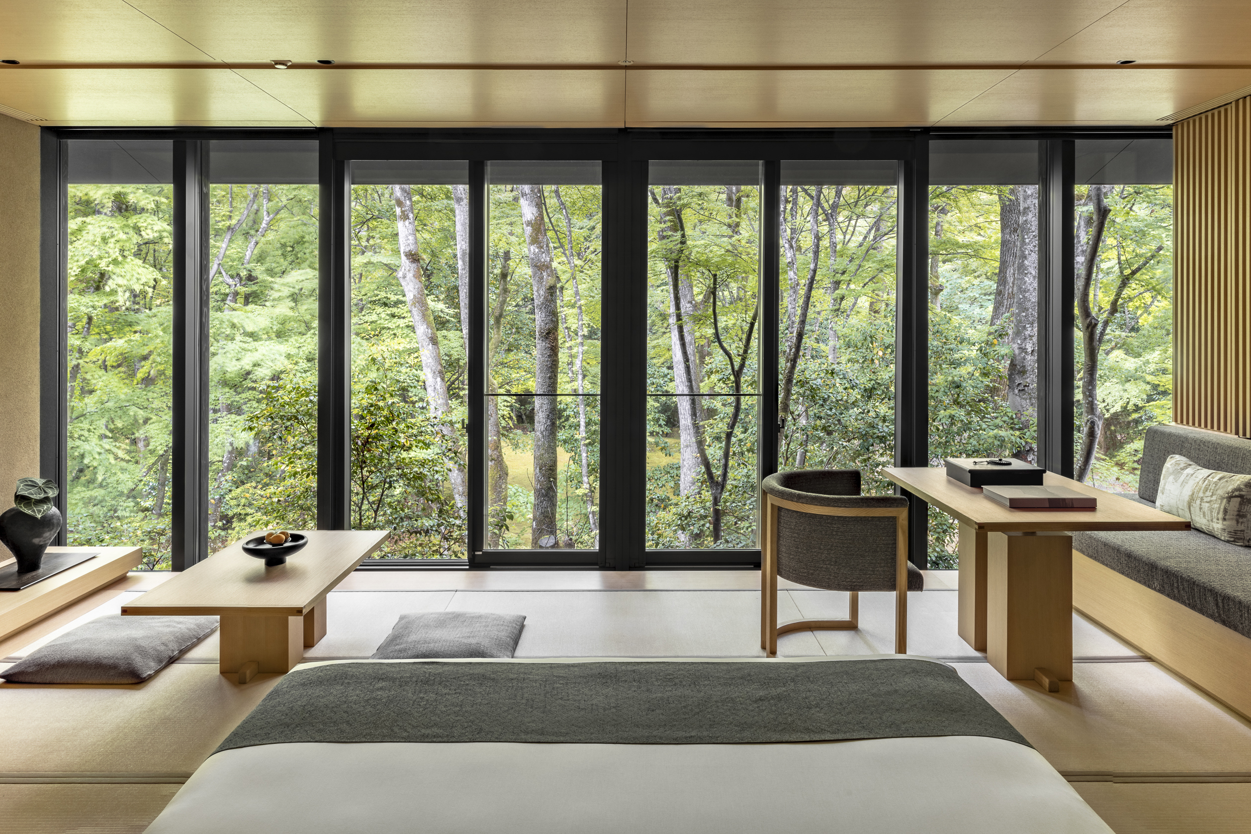 The Kaede Room at Aman Kyoto featuring stylish wooden furniture and a bed facing a large window that looks out over trees