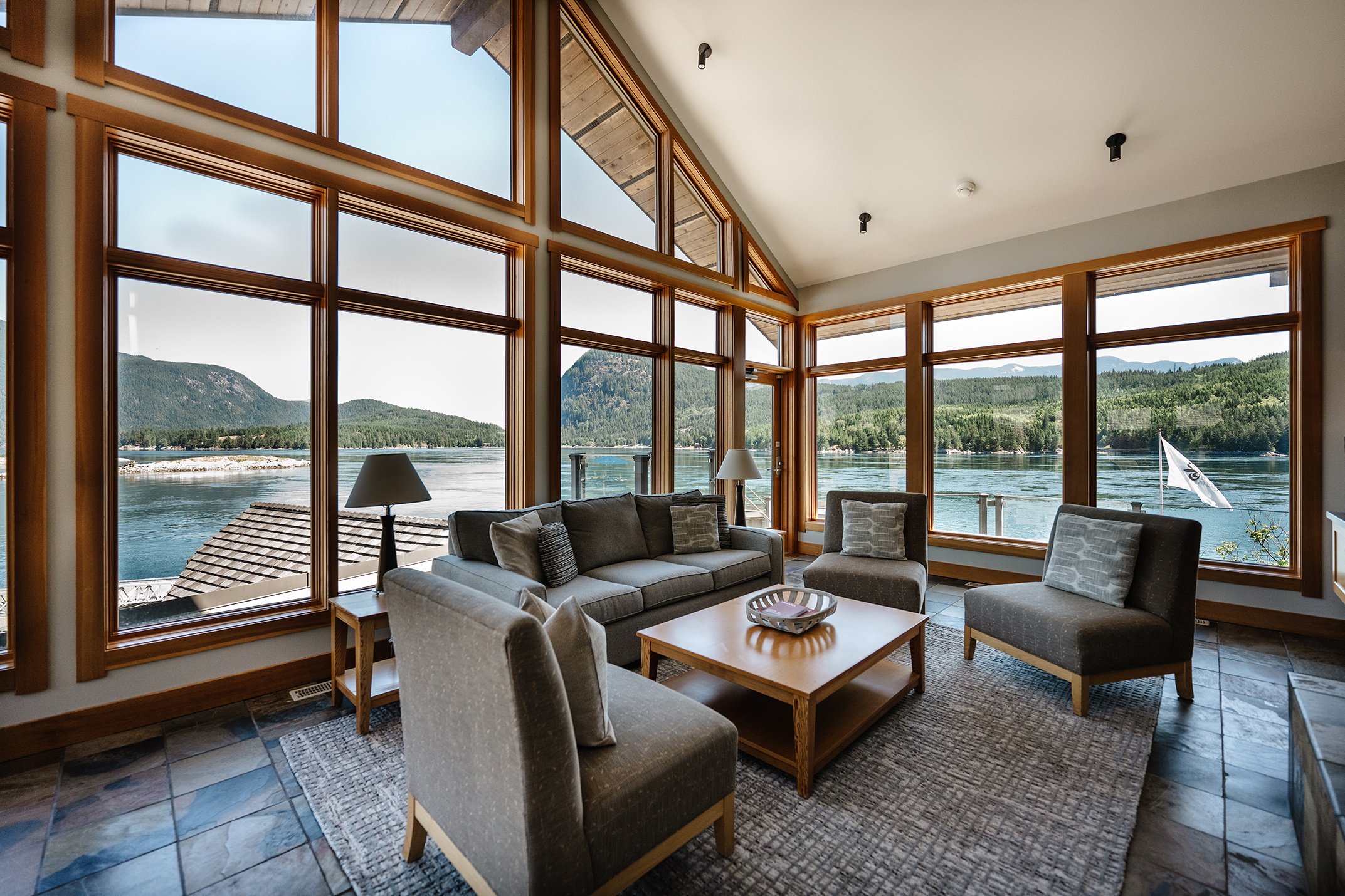 A vaulted room in Yuculta Lodge with floor to ceiling windows and a furniture set overlooking the lake and mountains