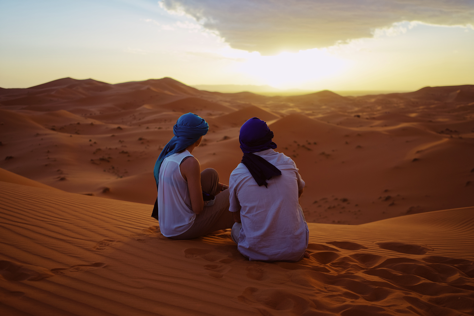 Two people sat on a dune in a desert