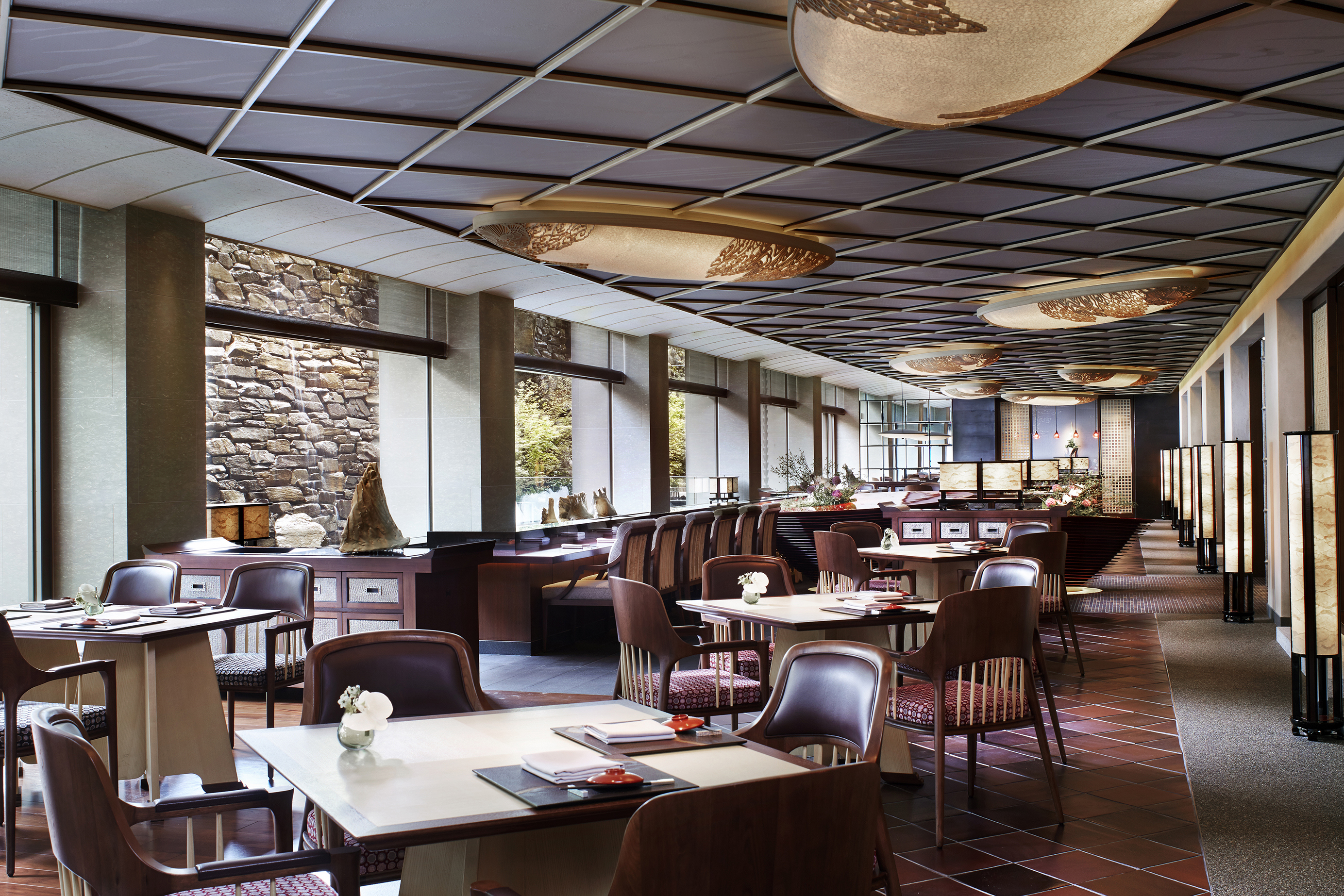 An ornate restaurant with plush dining tables and chairs beneath a decorative ceilings with ornamental light shades