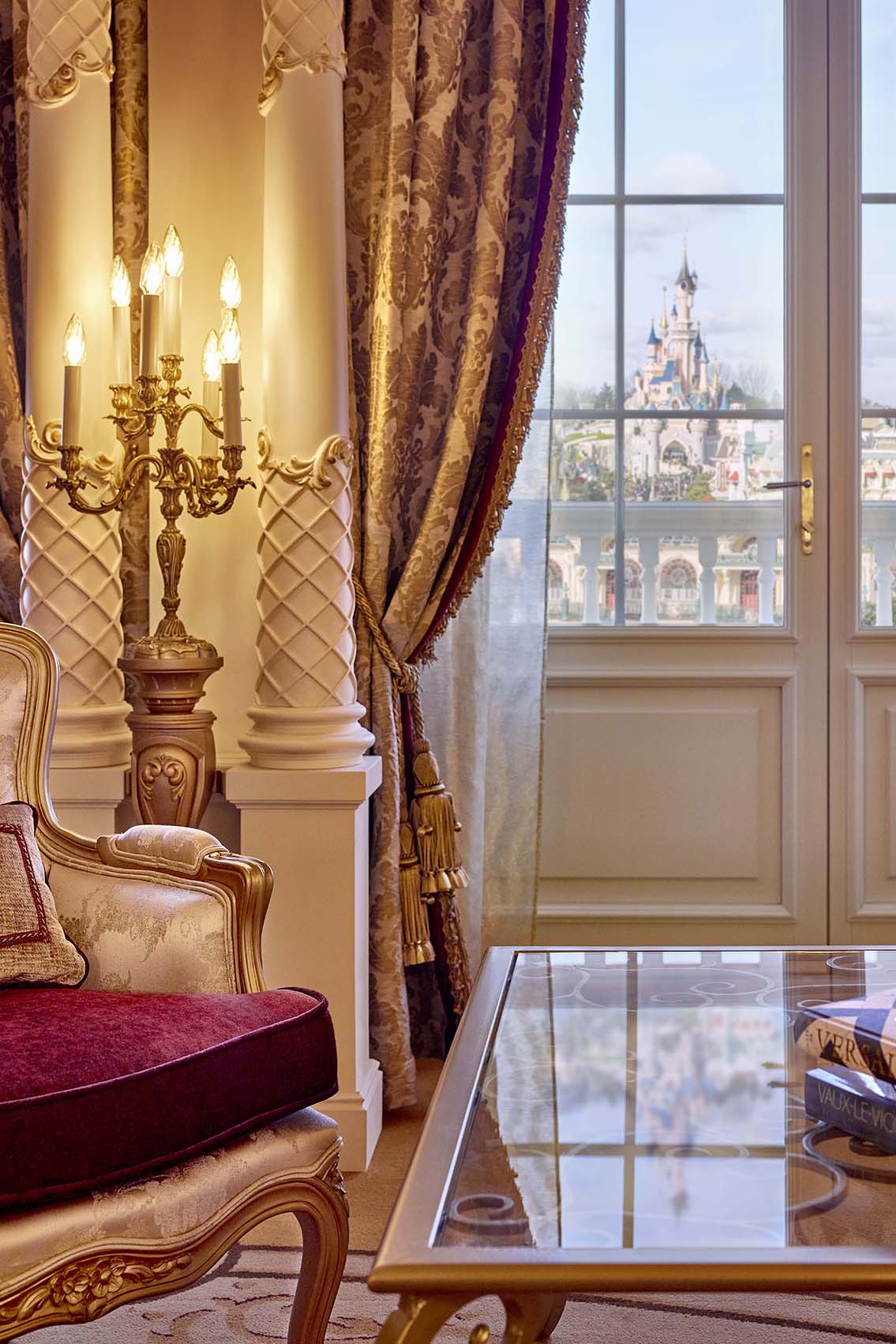 Europe, France, Paris, Disneyland® Hotel Princely Suite, close-up short of grand coffee table, armchair and electric candelabra, looking out throut double doors framed with gold curtains to the Disneyland® Sleeping Beauty castle