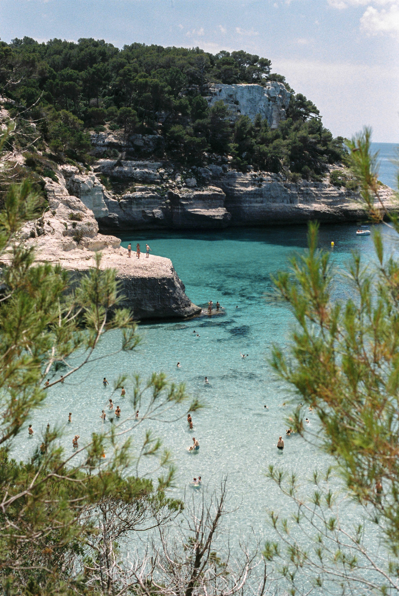 Swimmers and cliff jumpers at a rocky beach in Menorca