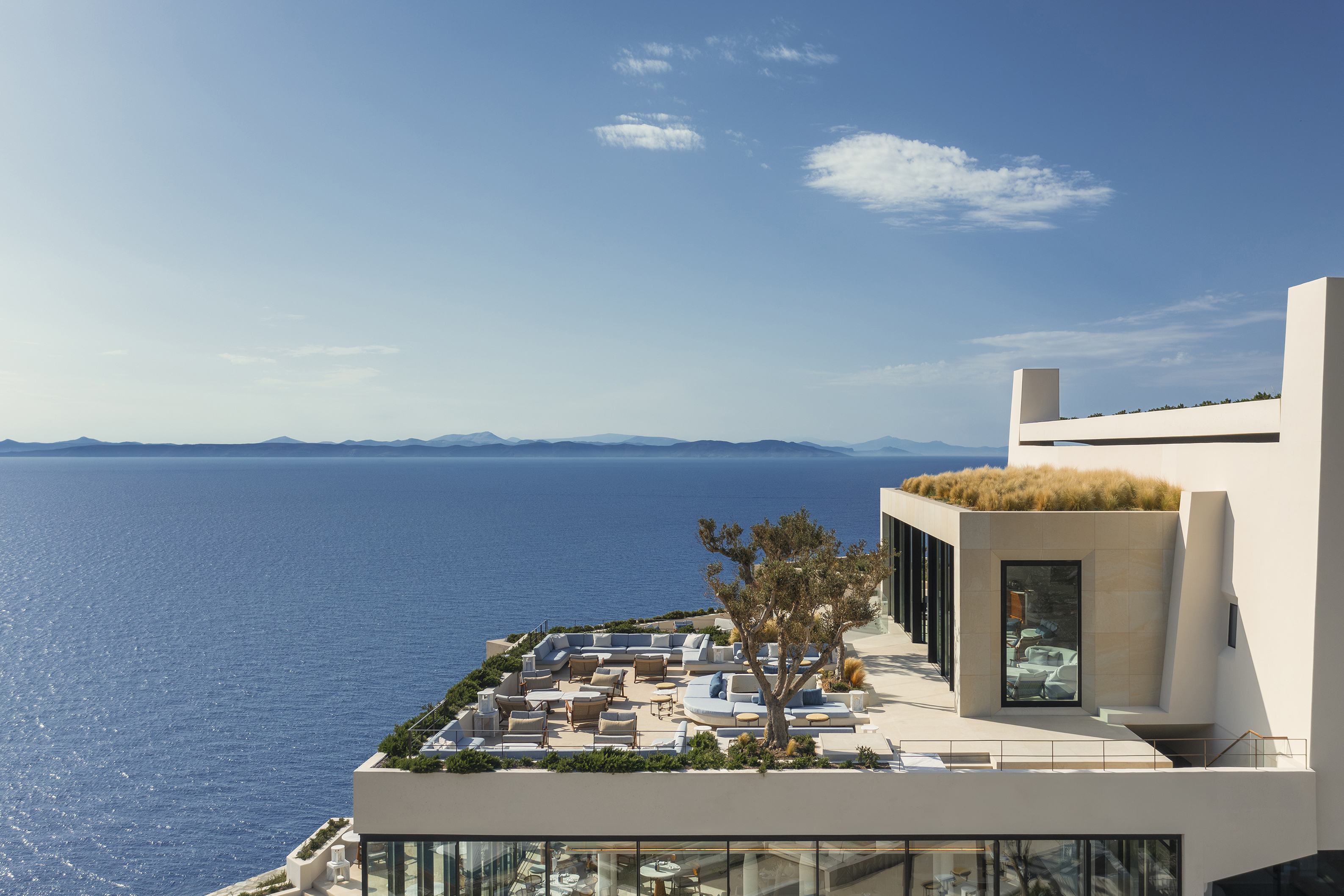 Outdoor terrace of Atria Restaurant filled with tables and olive trees looking out to sea