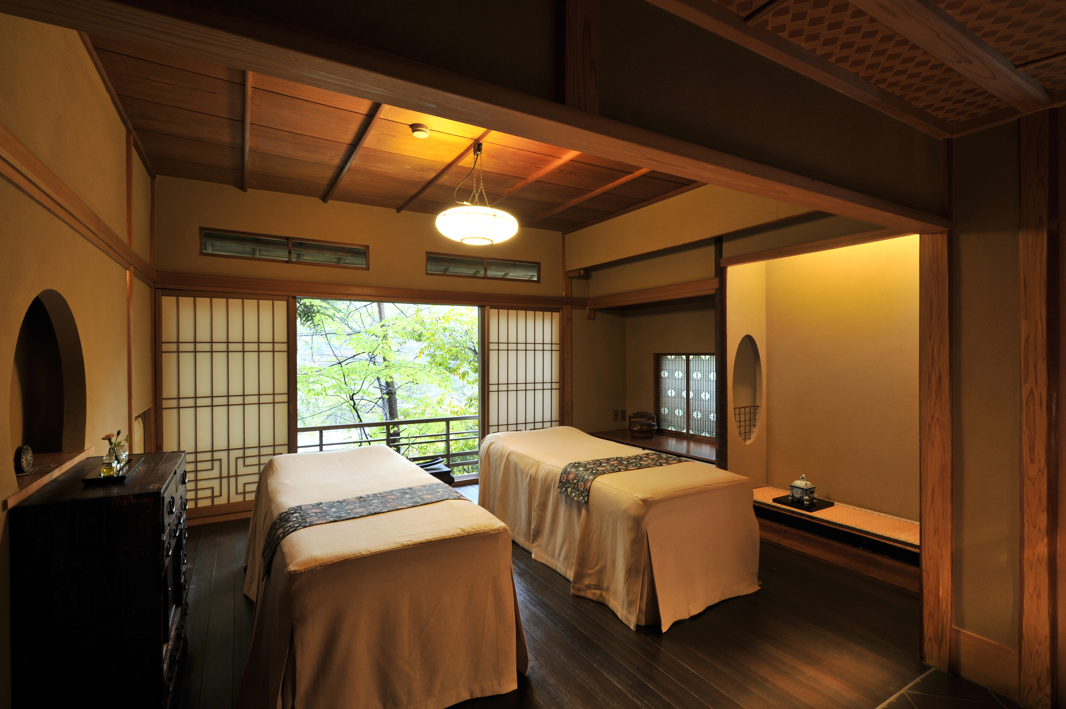 A cosy spa treatment room at Gora Kadan featuring two massage beds, traditional Japanese decor, and sliding doors looking out to the jungle