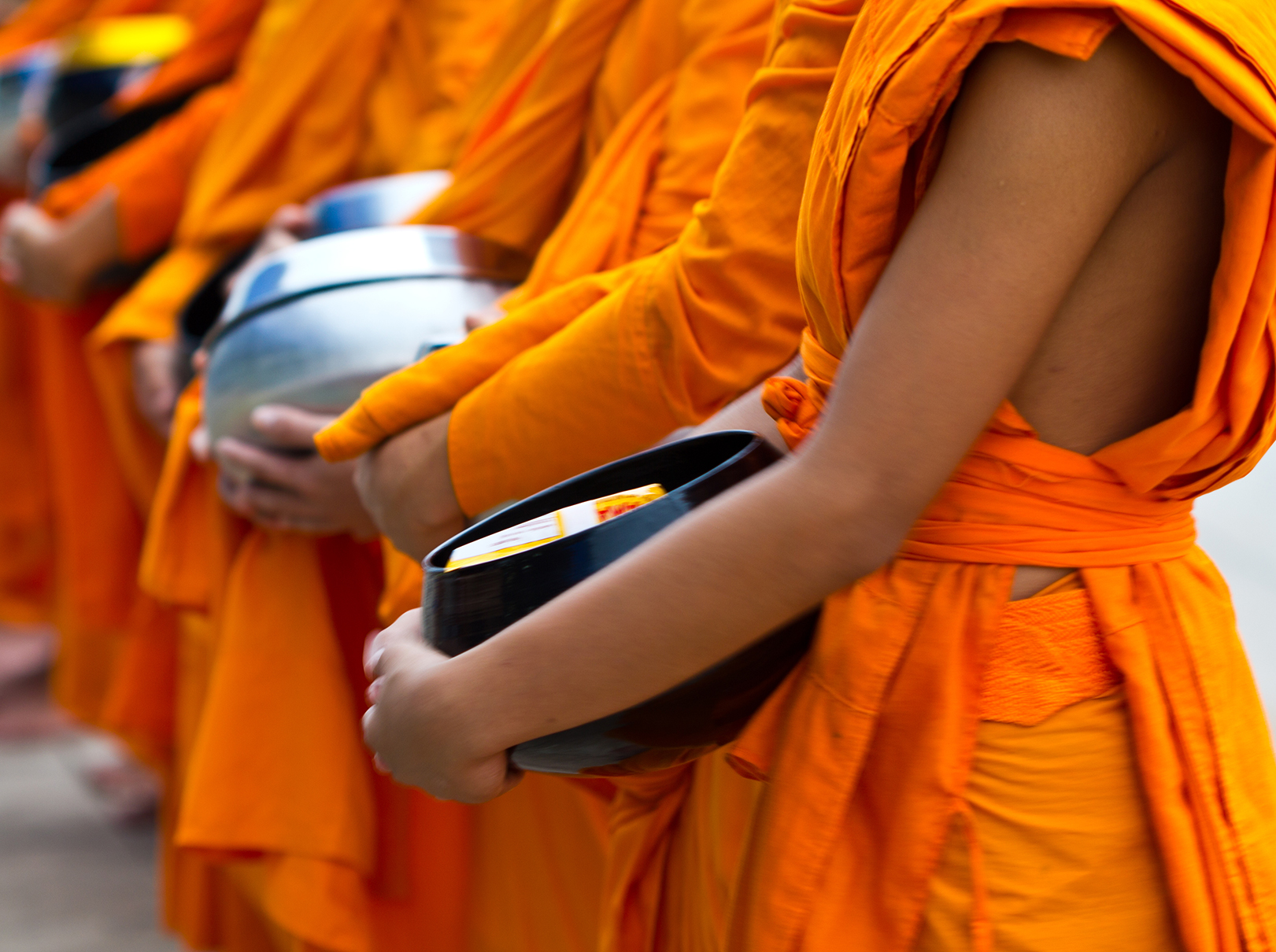 A line of monks wearing orange robes and holding circular pots