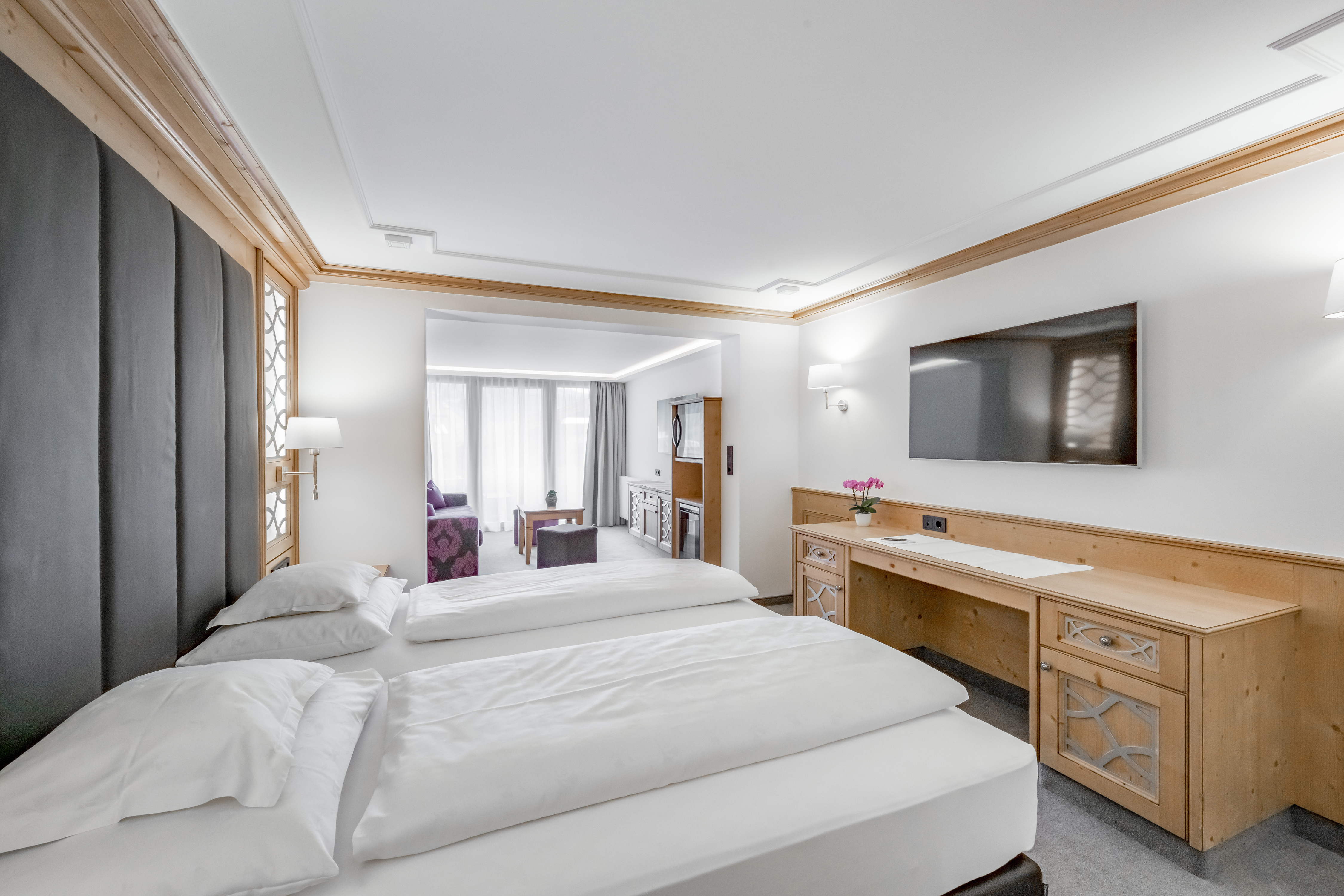 A spacious hotel room with two neatly made beds, a flat-screen TV, a wooden desk, and a sitting area with a sofa and large windows letting in natural light at Gourmet and Wine Hotel Austria