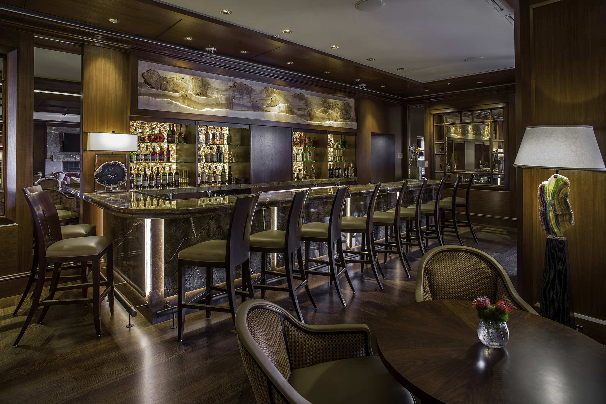 Elegant bar area at Duchin Lounge with a long marble counter, high-backed chairs, and shelves filled with bottles behind the bar