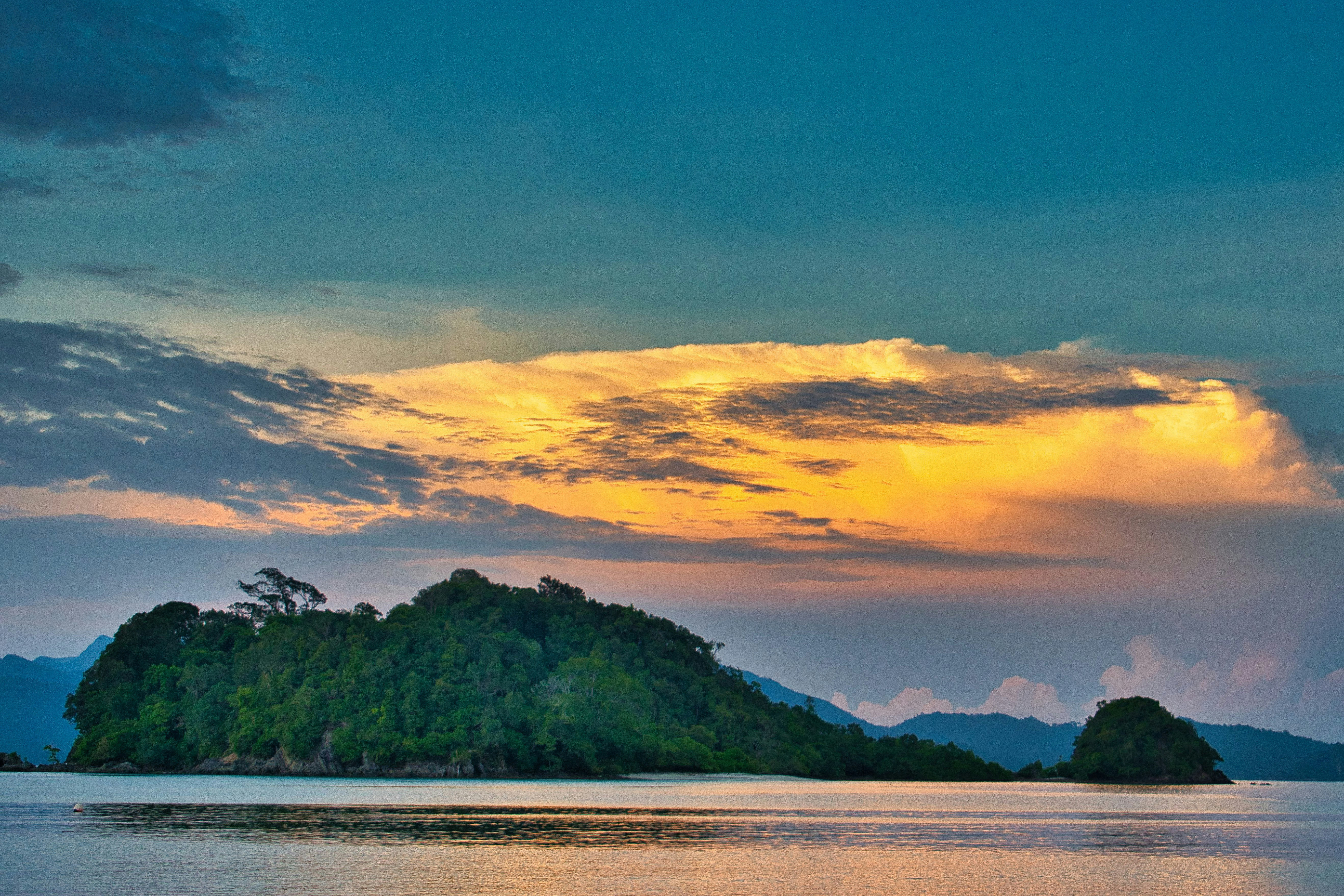 A grenn island in the Lanhkawi archipeligo beneath a golden sky