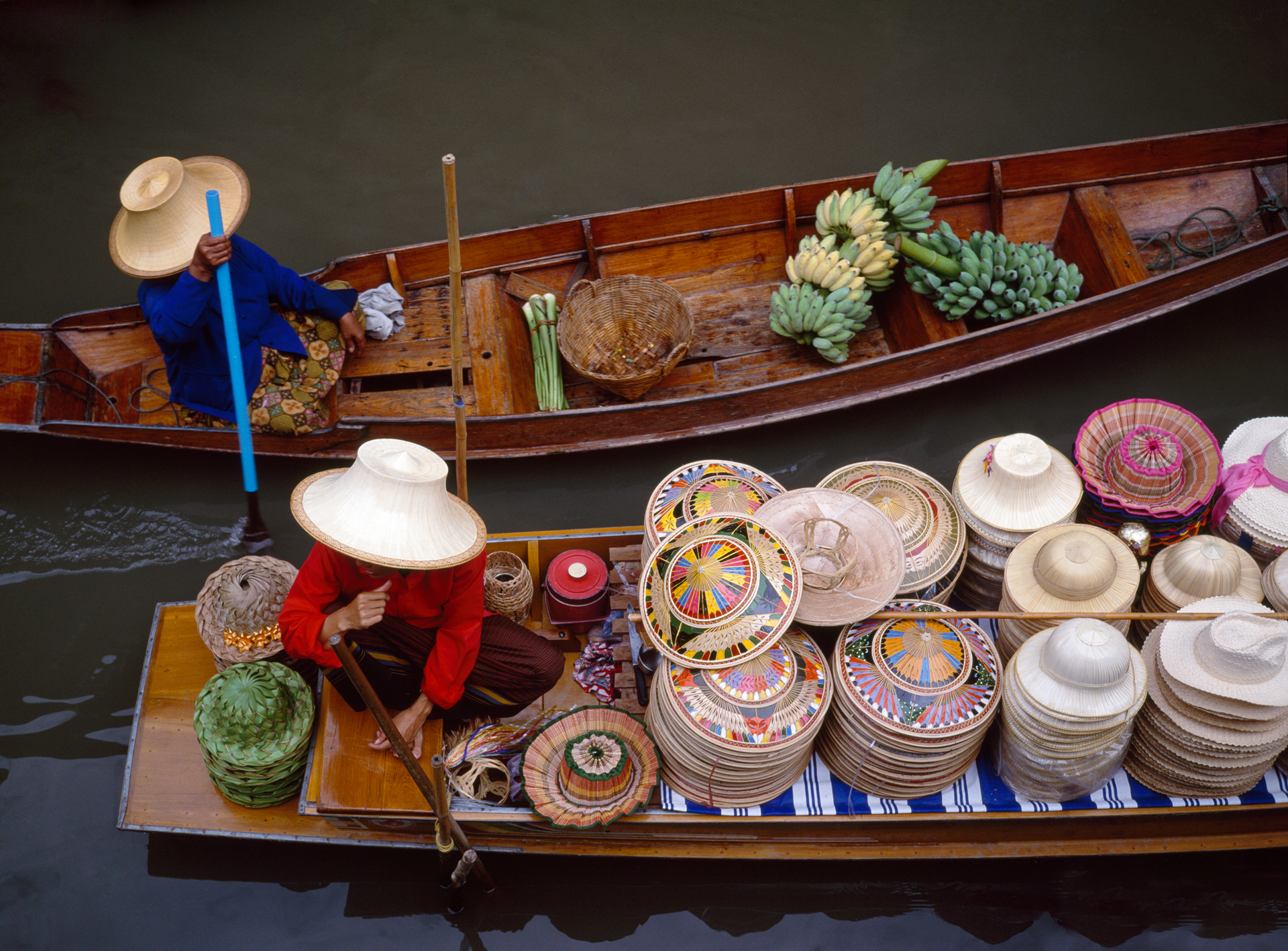 Two boats from the Damnoen Saduak Floating Market with one having fruit and another with hats