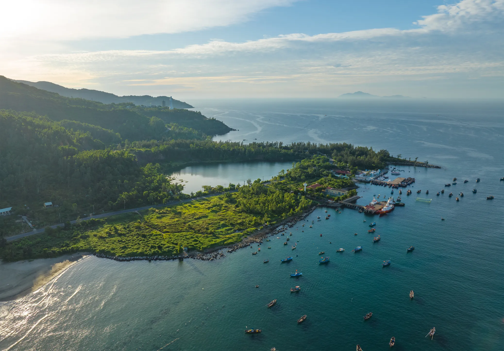 Aerial view of Son Tra Peninsula with verdant hills, a peaceful coastline, and boats scattered across turquoise waters.