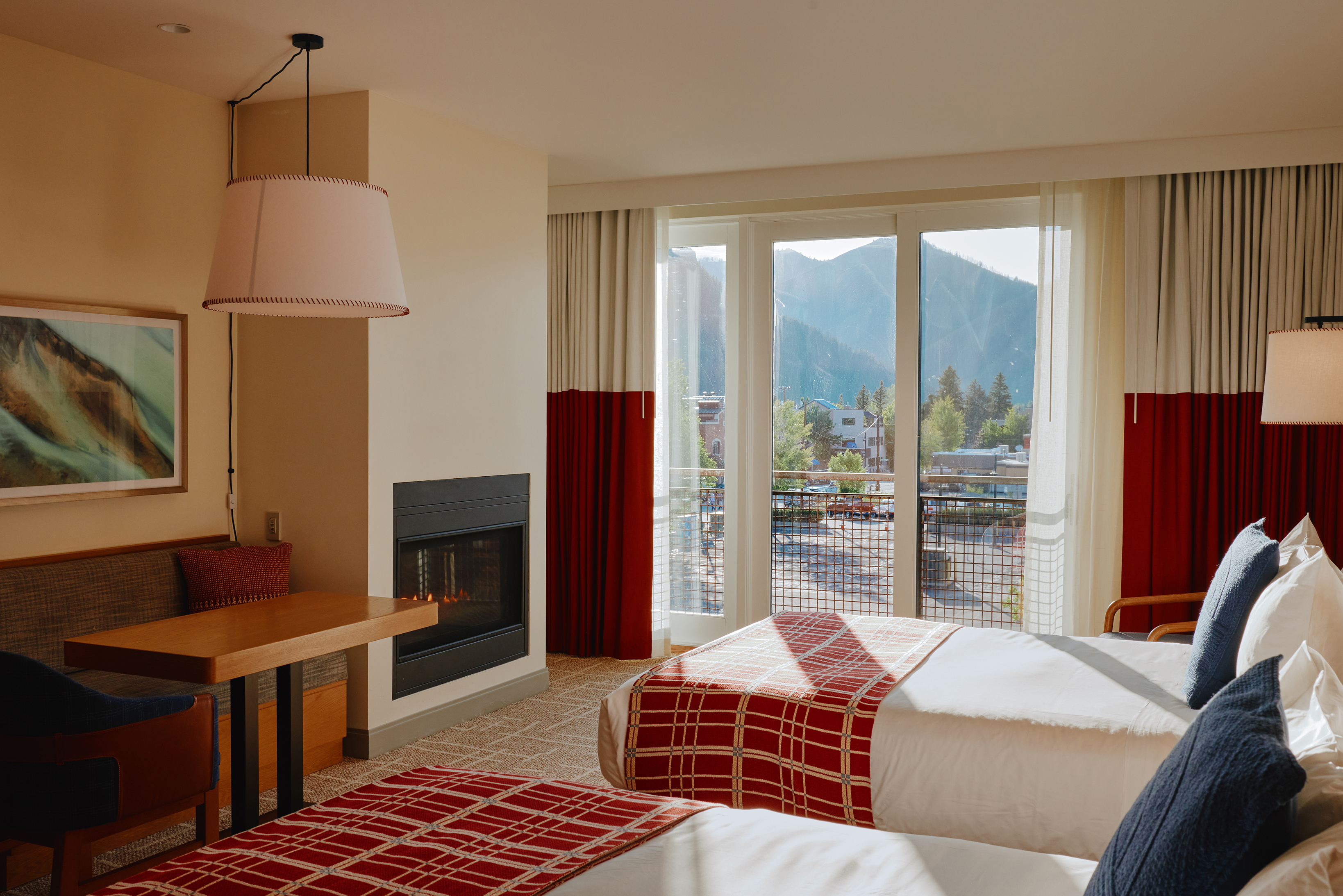 A hotel room at Limelight Ketchum featuring two beds, a fireplace, a desk, and a large window with a scenic mountain view