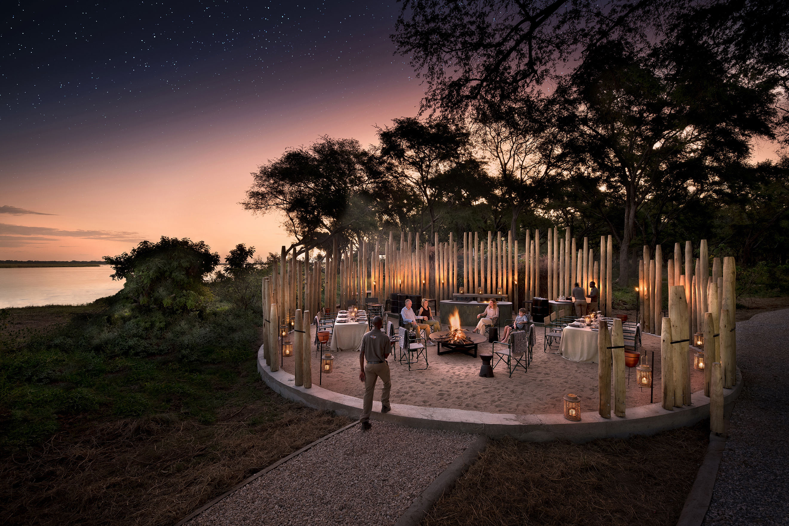 A waiter taking drinks to people sat in the boma at Lolebezi at dusk