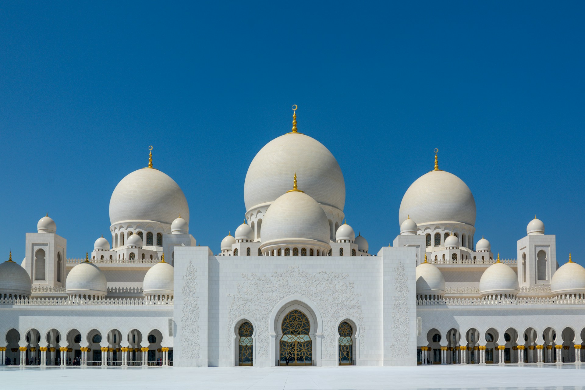 Sheikh Zayed Grand Mosque in Abu Dhabi with multiple large white domes and intricate architectural details against a clear blue sky