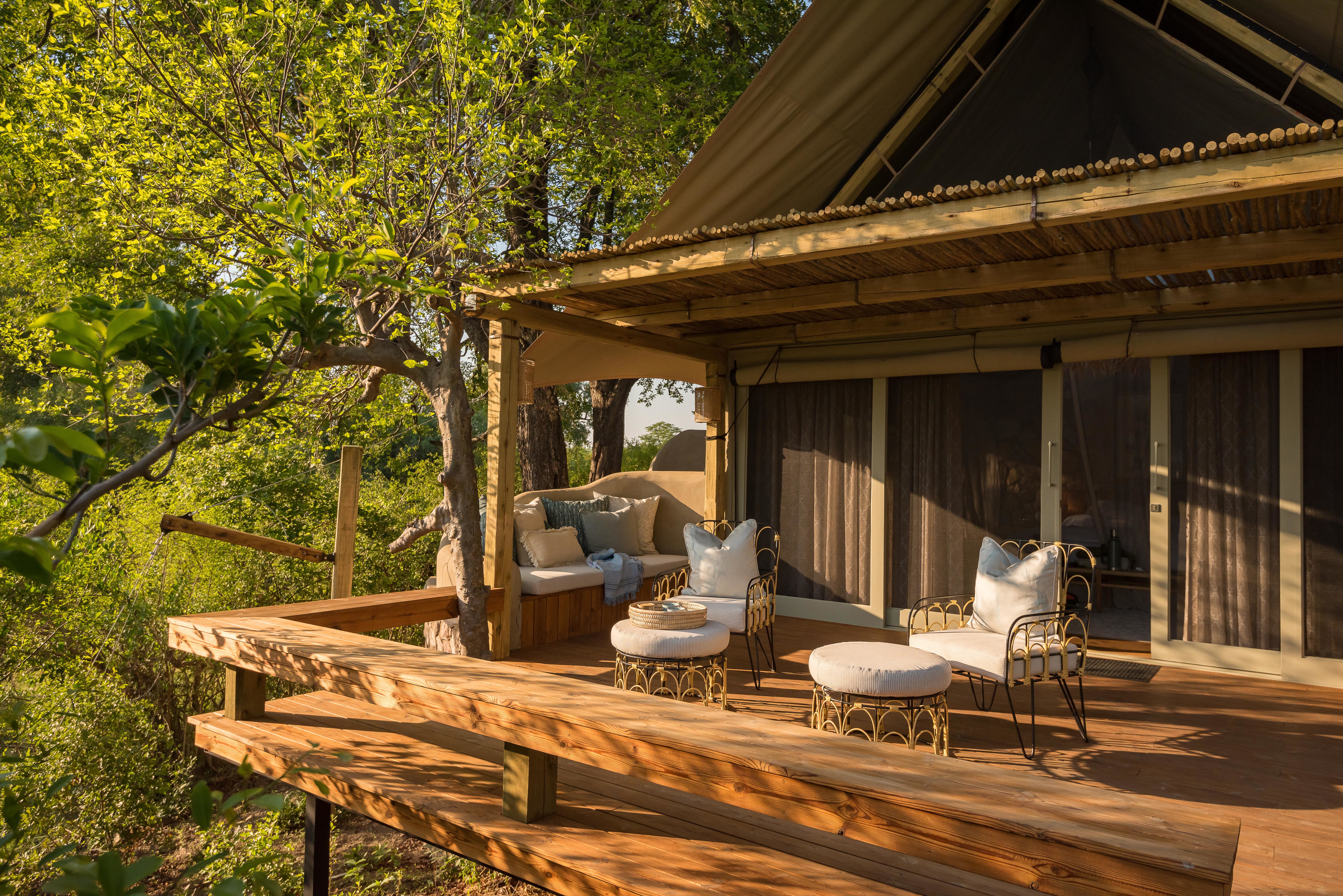The outdoor deck of a suite surrounded by trees, featuring a woven furniture set bathed in sunlight
