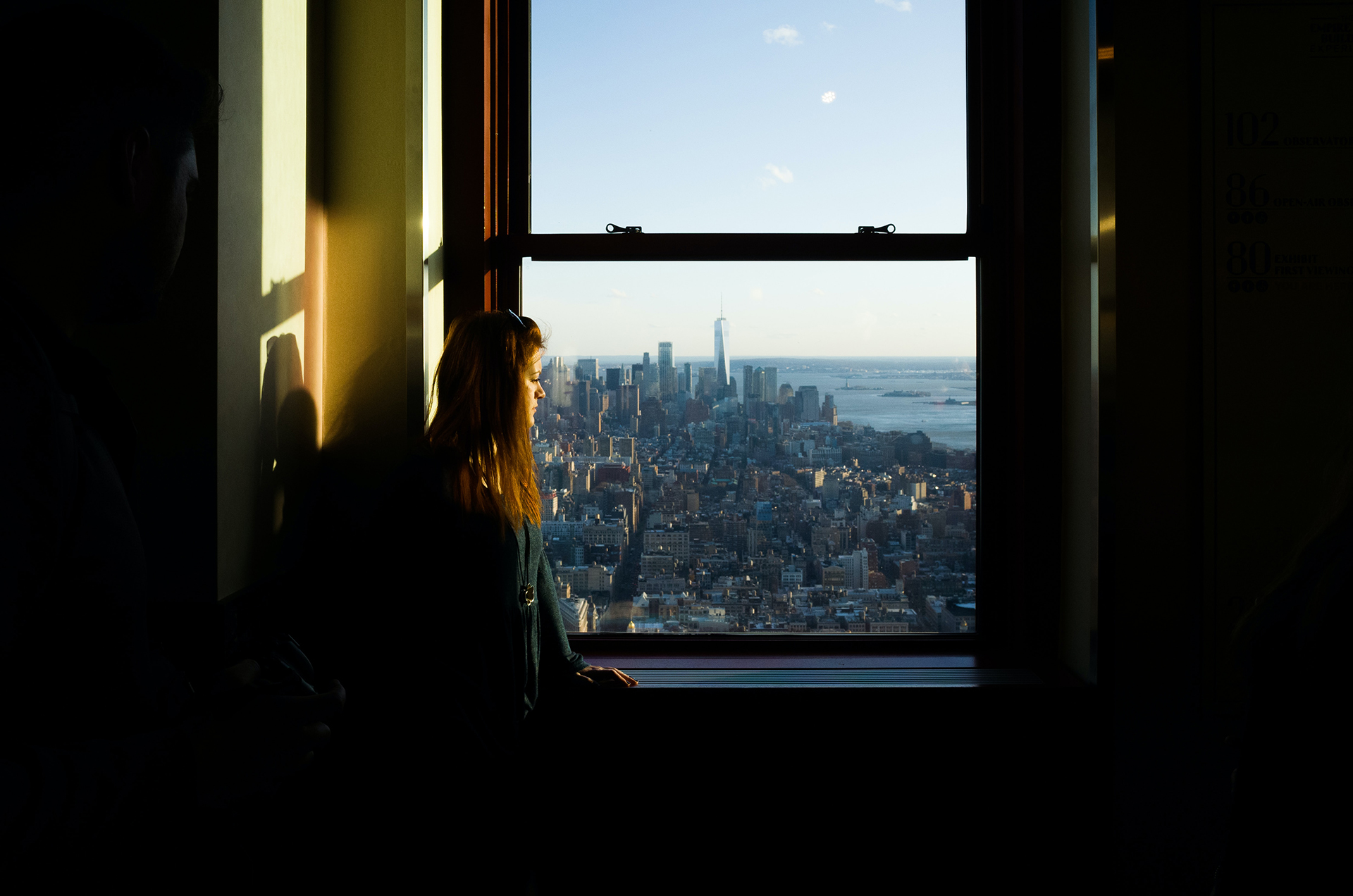 A woman looking out of a high rise building window towards the New York skyline