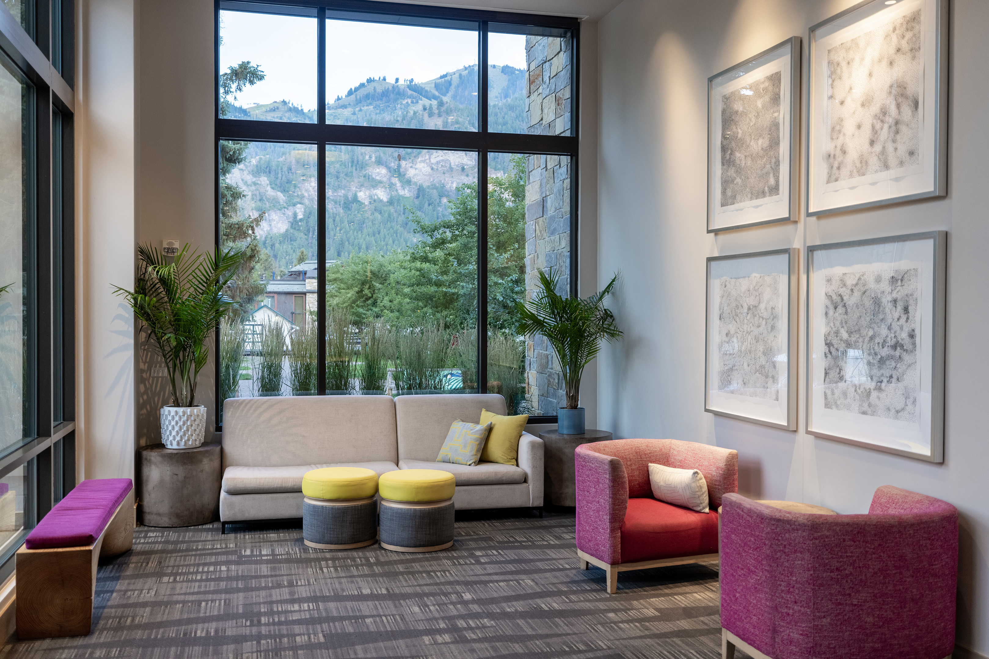 A cosy lounge at Limelight Ketchum hotel with modern furniture, a central glass-enclosed fireplace, and large windows revealing an evening outdoor view
