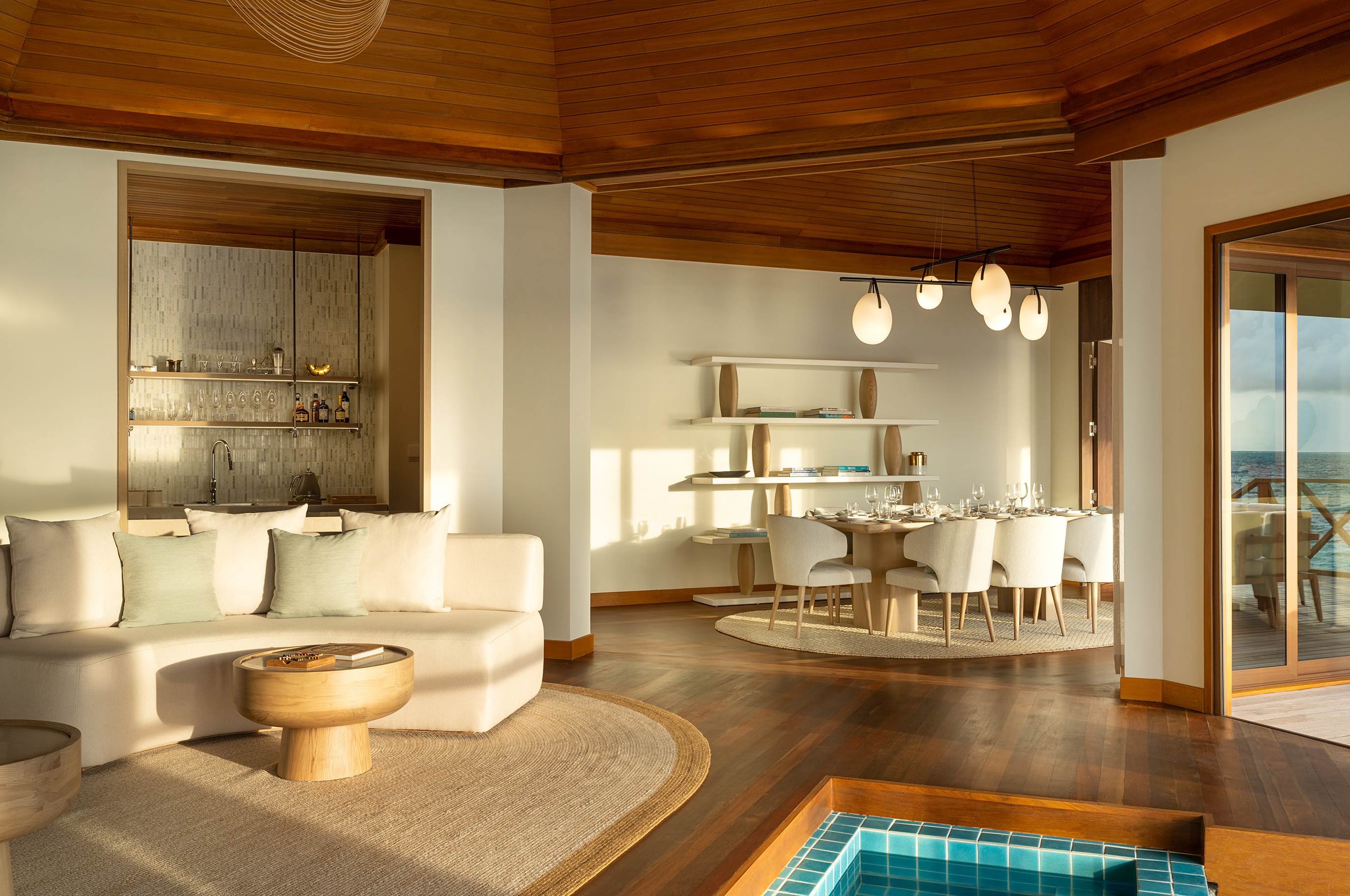 Two Bedroom Ocean Pavilion lounge featuring pale furniture under a beamed ceiling with natural decor and a glimpse of the indoor plunge pool