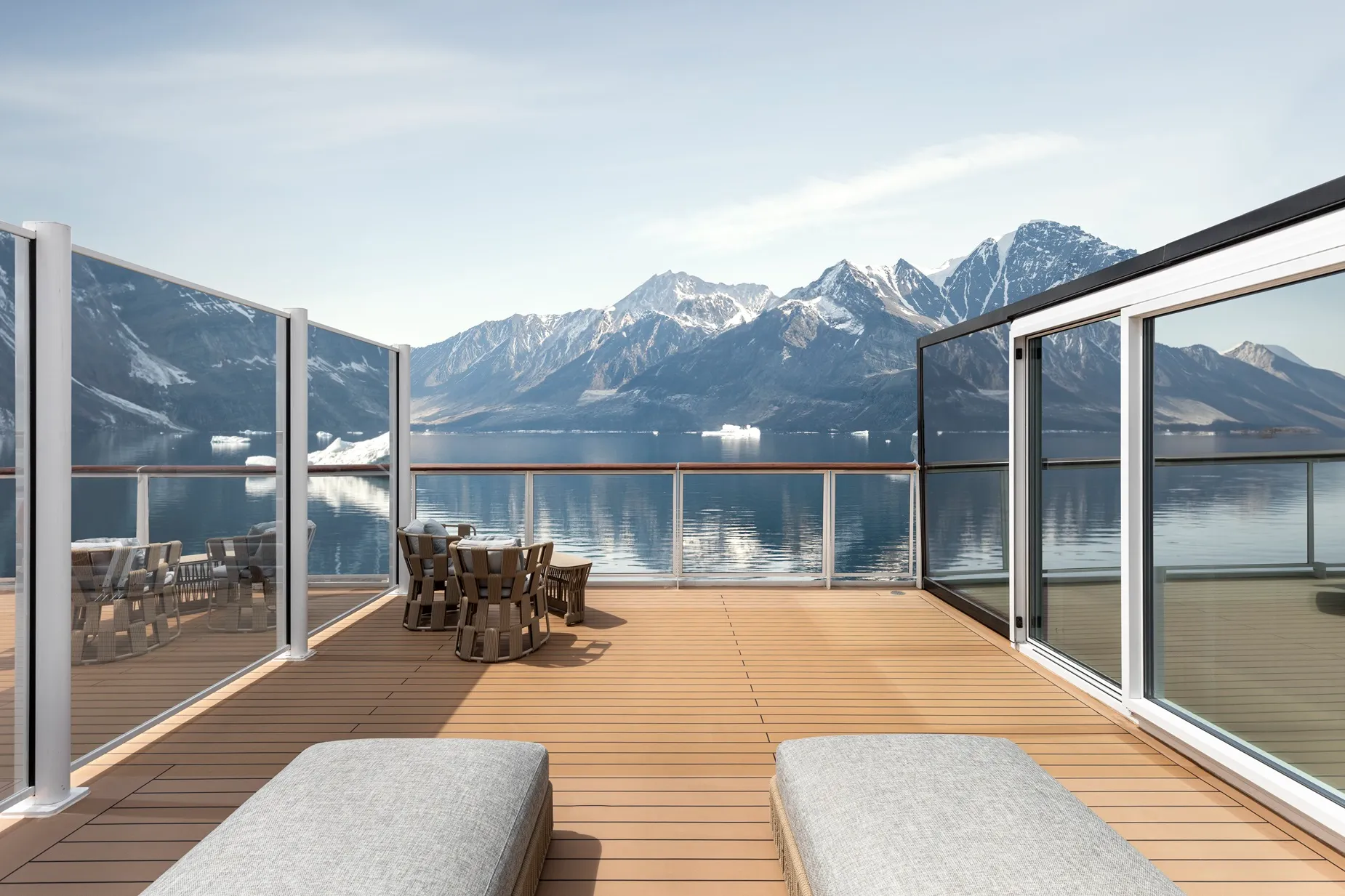 A spacious deck with lounge chairs and a dining table overlooking a serene lake and snow-capped mountains.