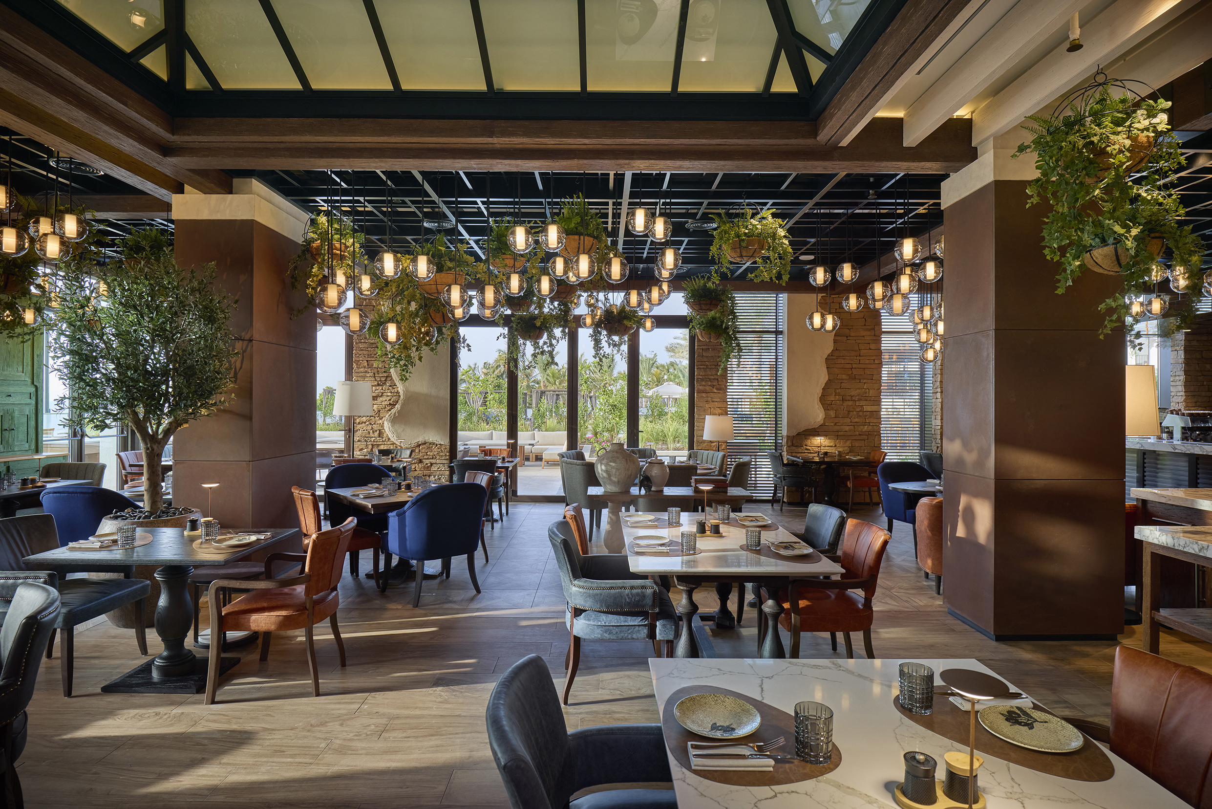 Essenza Restaurant at Mandarin Oriental Muscat featuring tables set for dinner beneath a ceiling covered in greenery and lanterns